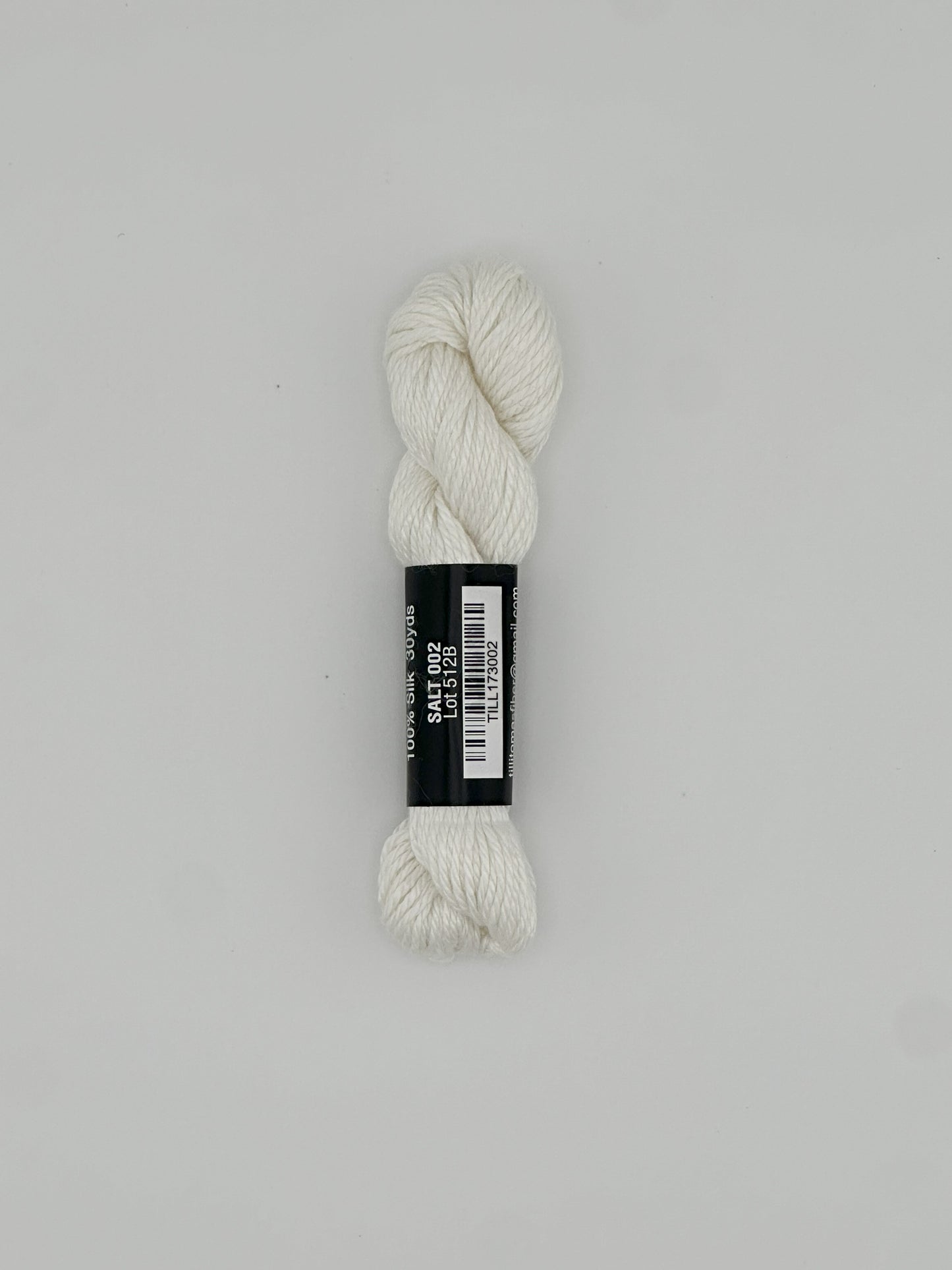 30 yard skein of Pepper Pot Silk needlepoint thread in salt 002 white, with black and white label lying flat on white background