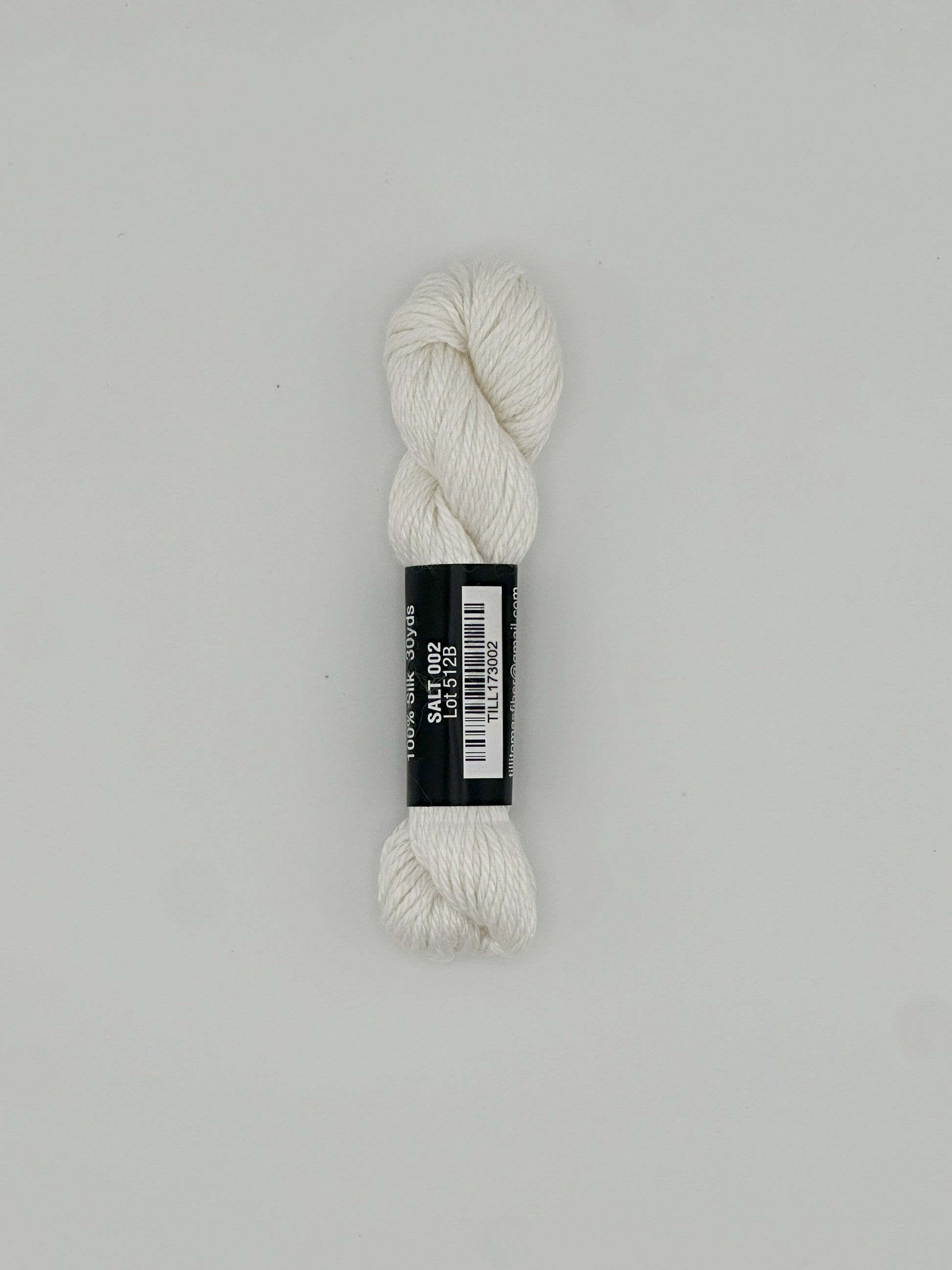30 yard skein of Pepper Pot Silk needlepoint thread in salt 002 white, with black and white label lying flat on white background