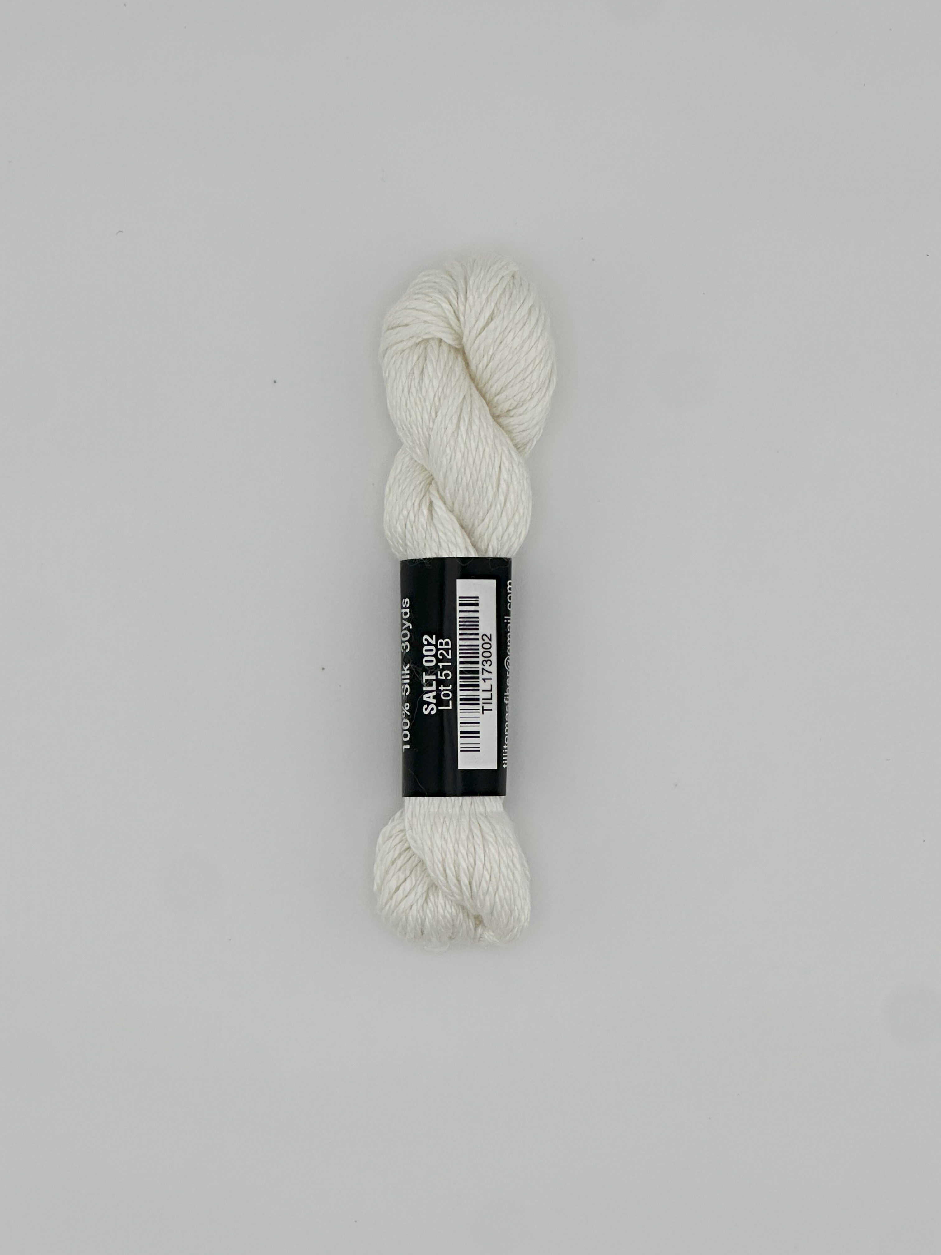 30 yard skein of Pepper Pot Silk needlepoint thread in salt 002 white, with black and white label lying flat on white background