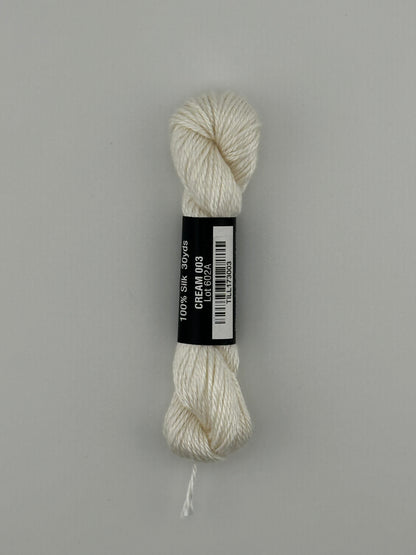 30 yard skein of Pepper Pot Silk needlepoint thread in cream 003, with black and white label lying flat on white background