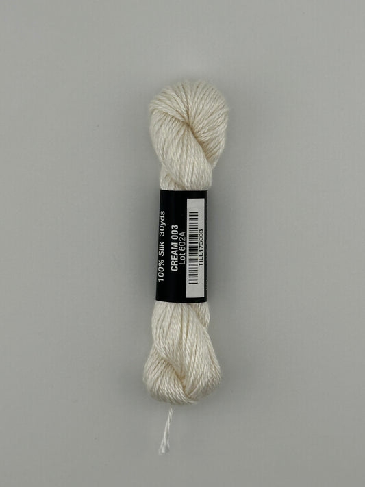 30 yard skein of Pepper Pot Silk needlepoint thread in cream 003, with black and white label lying flat on white background