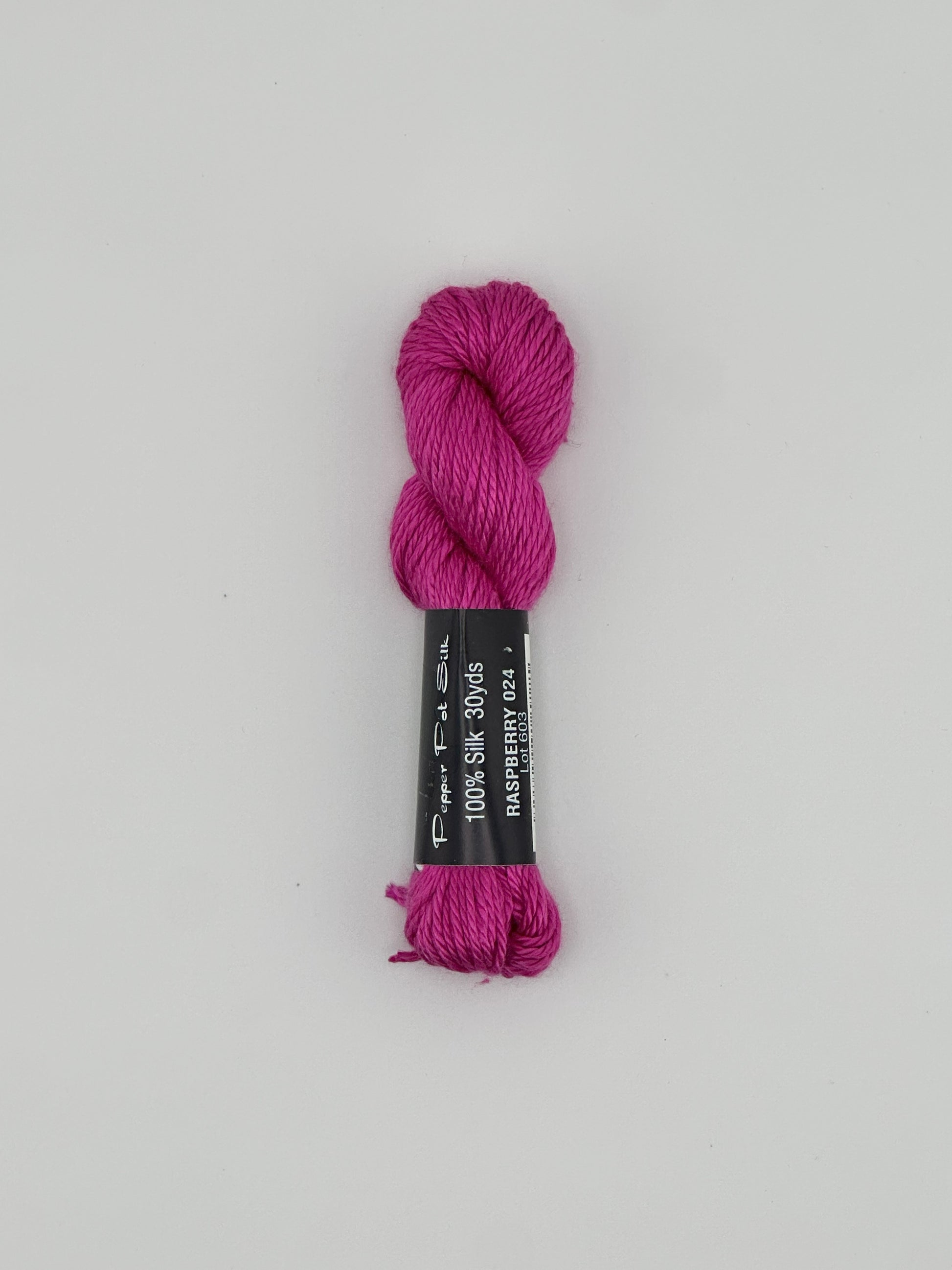 30 yard skein of Pepper Pot Silk needlepoint thread in raspberry pink 024 with black and white label lying flat on white background