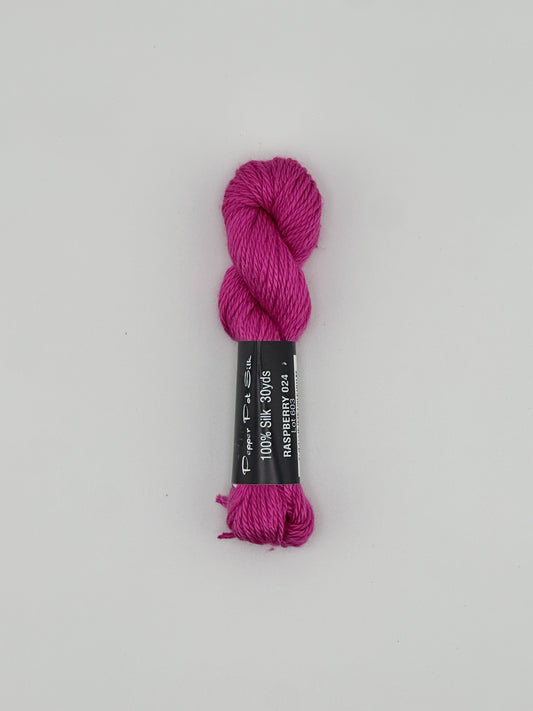 30 yard skein of Pepper Pot Silk needlepoint thread in raspberry pink 024 with black and white label lying flat on white background