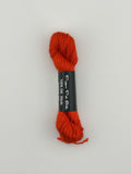 30 yard skein of Pepper Pot Silk needlepoint thread in orange 033, with black and white label lying flat on white background
