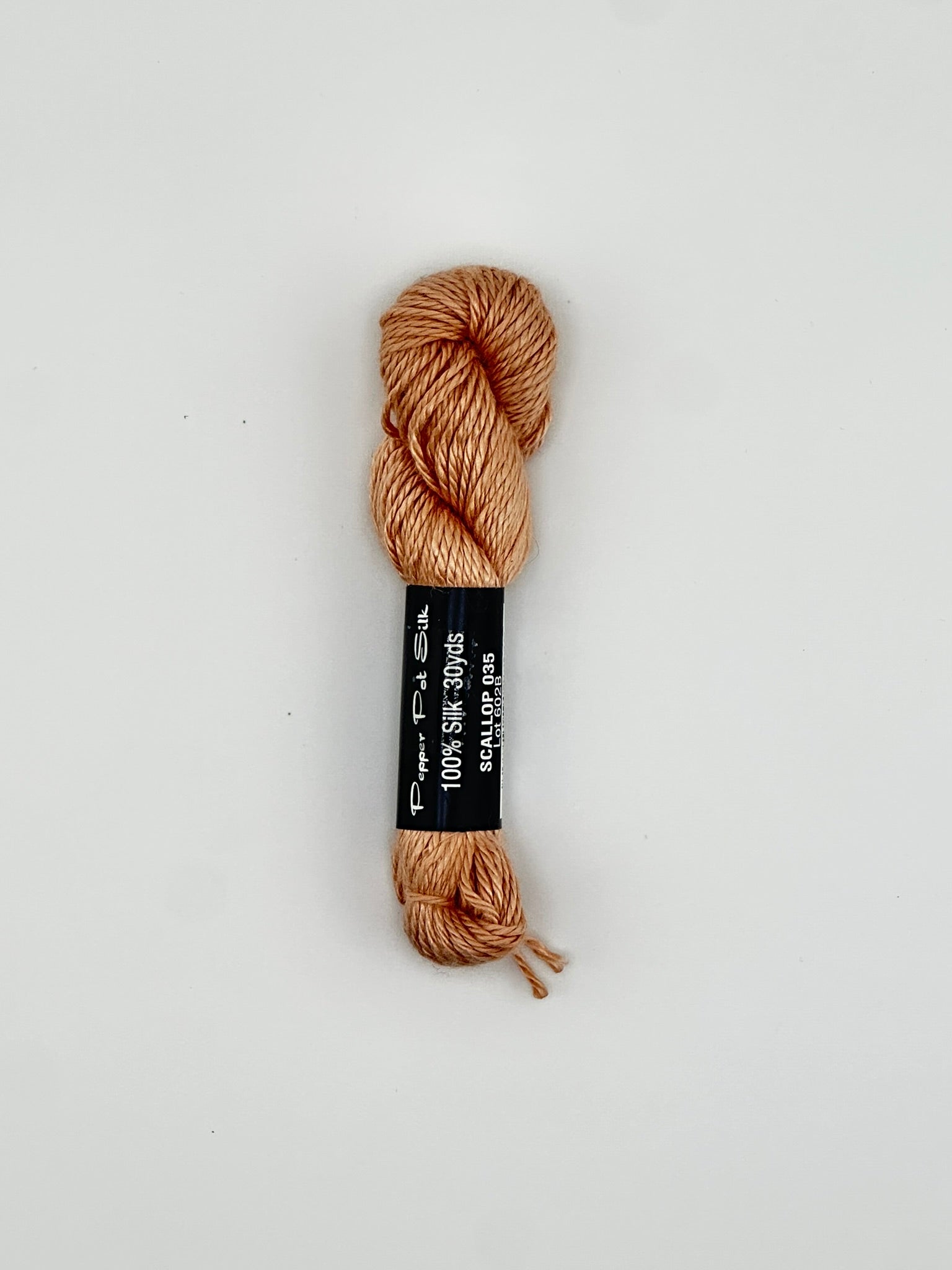 30 yard skein of Pepper Pot Silk needlepoint thread in callop 035 with black and white label lying flat on white background