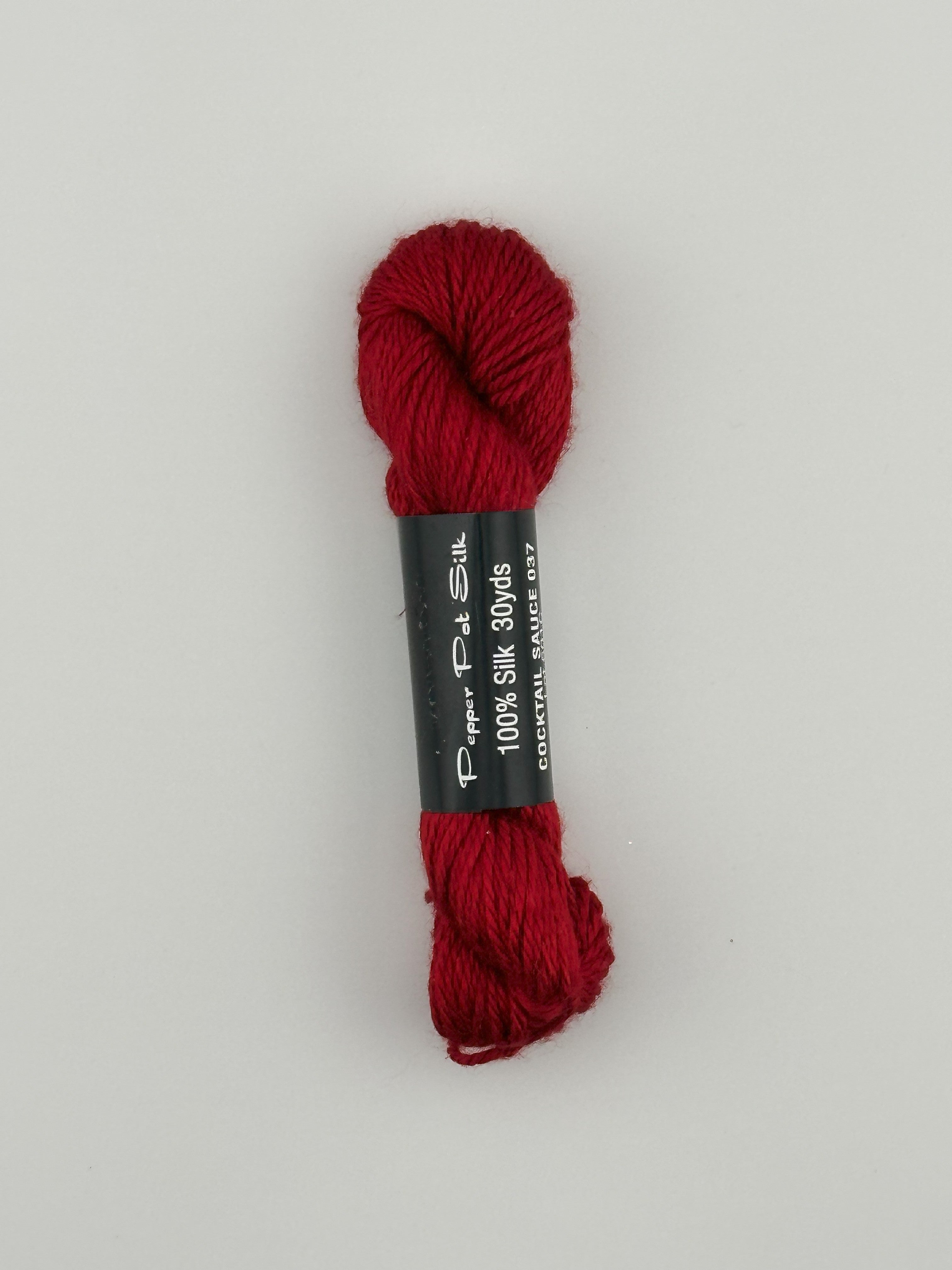 30 yard skein of Pepper Pot Silk needlepoint thread in cocktail sauce 037 red, with black and white label lying flat on white background