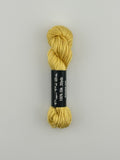 30 yard skein of Pepper Pot Silk needlepoint thread in banana 045 yellow, with black and white label lying flat on white background