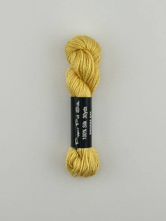 30 yard skein of Pepper Pot Silk needlepoint thread in banana 045 yellow, with black and white label lying flat on white background