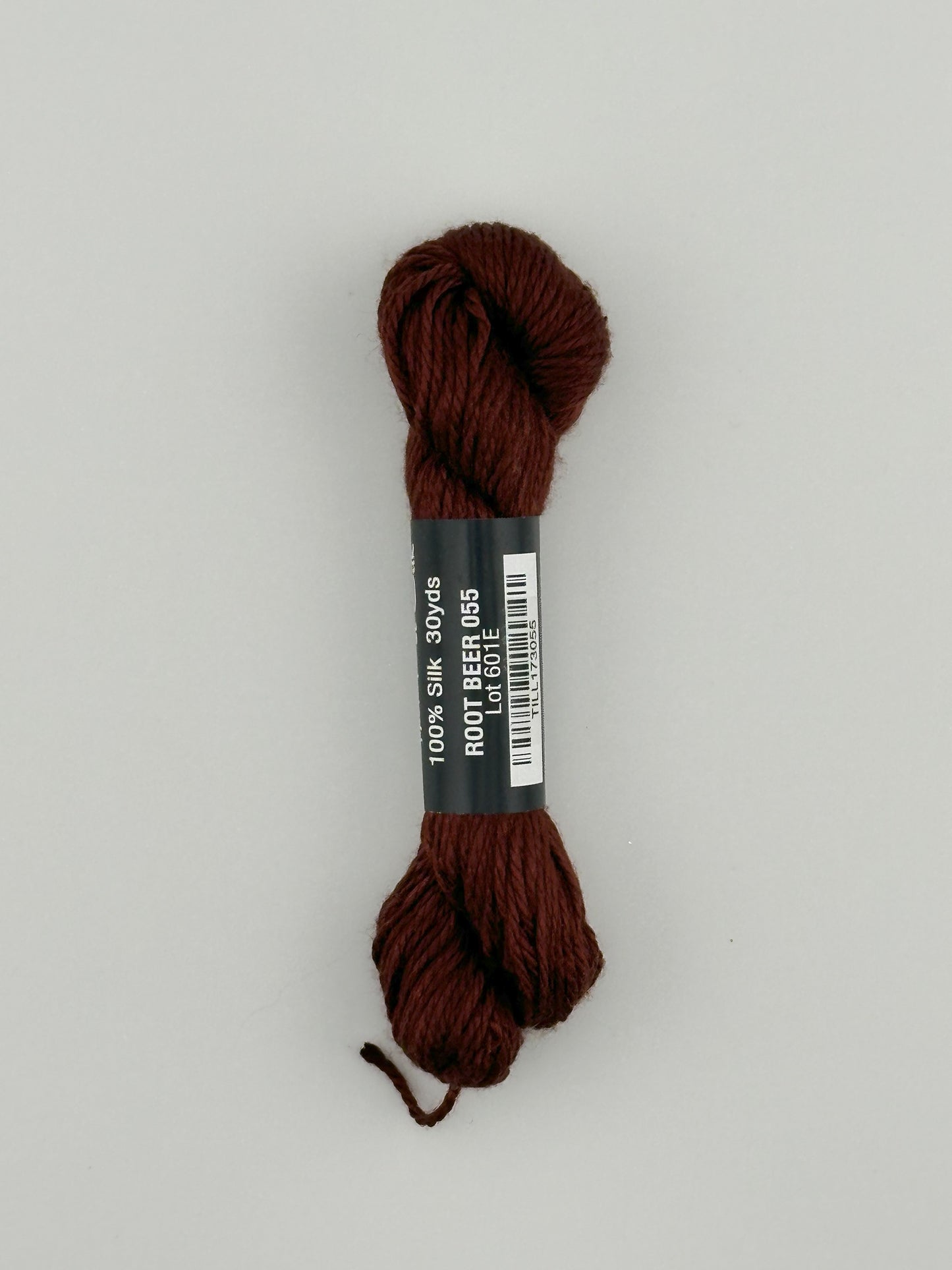 30 yard skein of Pepper Pot Silk needlepoint thread in root beer 055 brown, with black and white label lying flat on white background