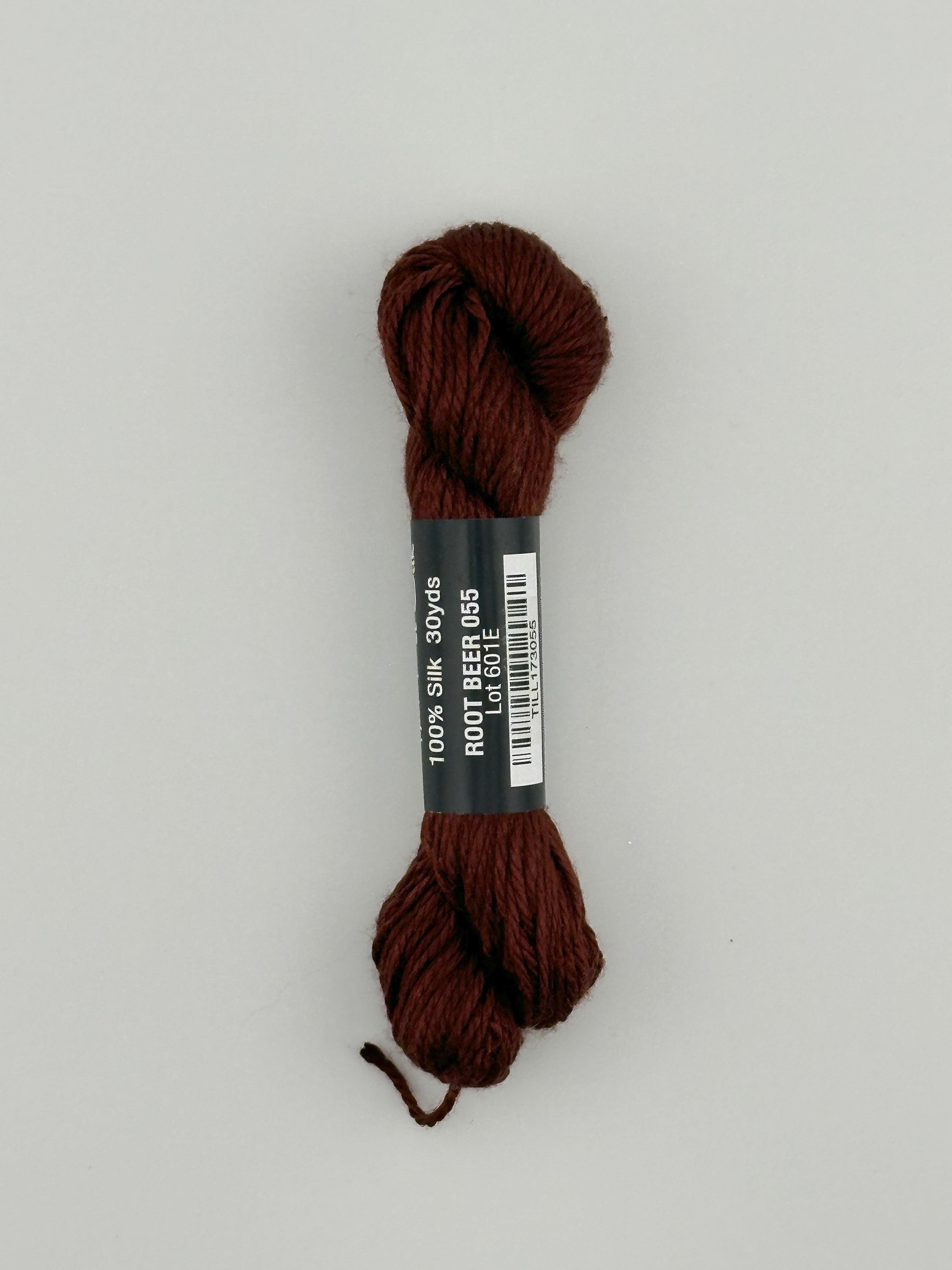 30 yard skein of Pepper Pot Silk needlepoint thread in root beer 055 brown, with black and white label lying flat on white background