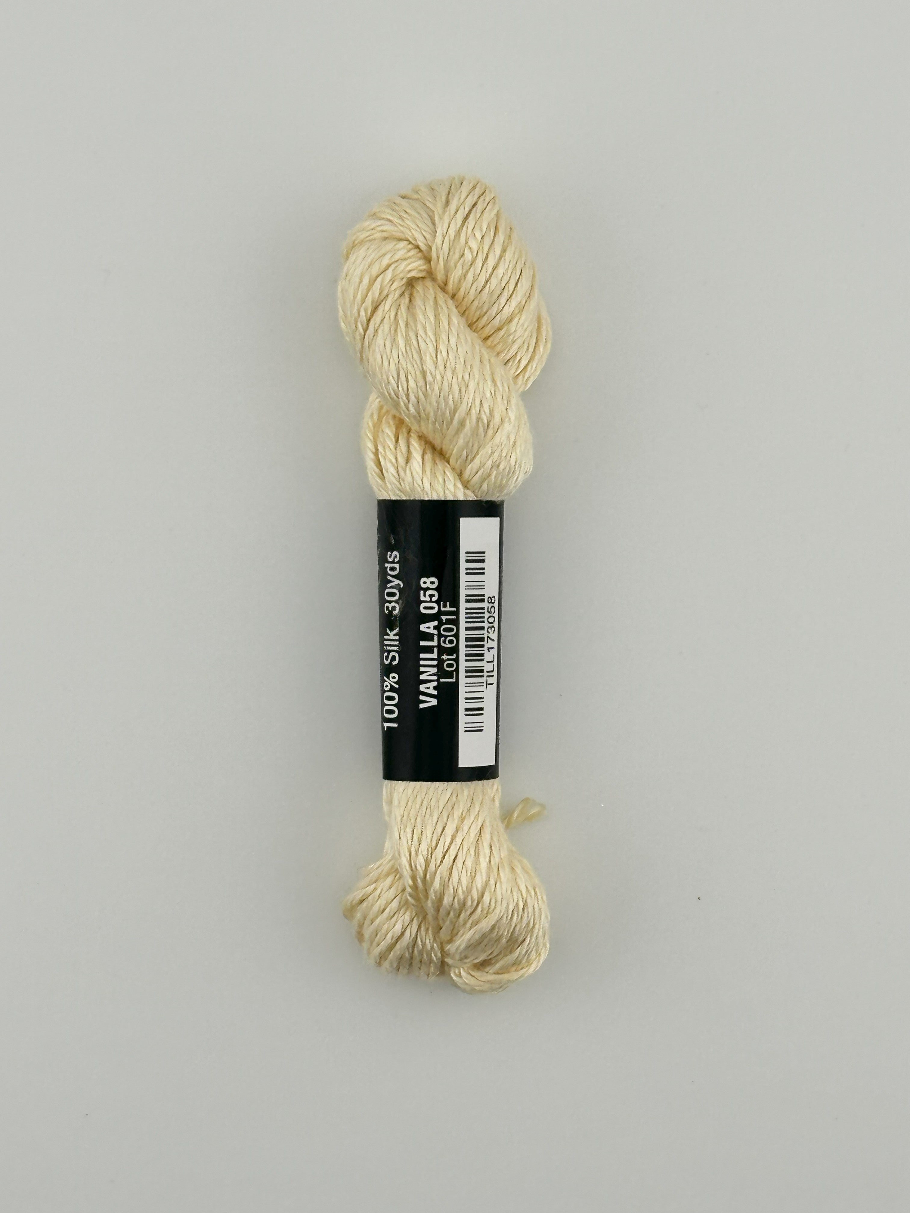 30 yard skein of Pepper Pot Silk needlepoint thread in vanilla 058, with black and white label lying flat on white background
