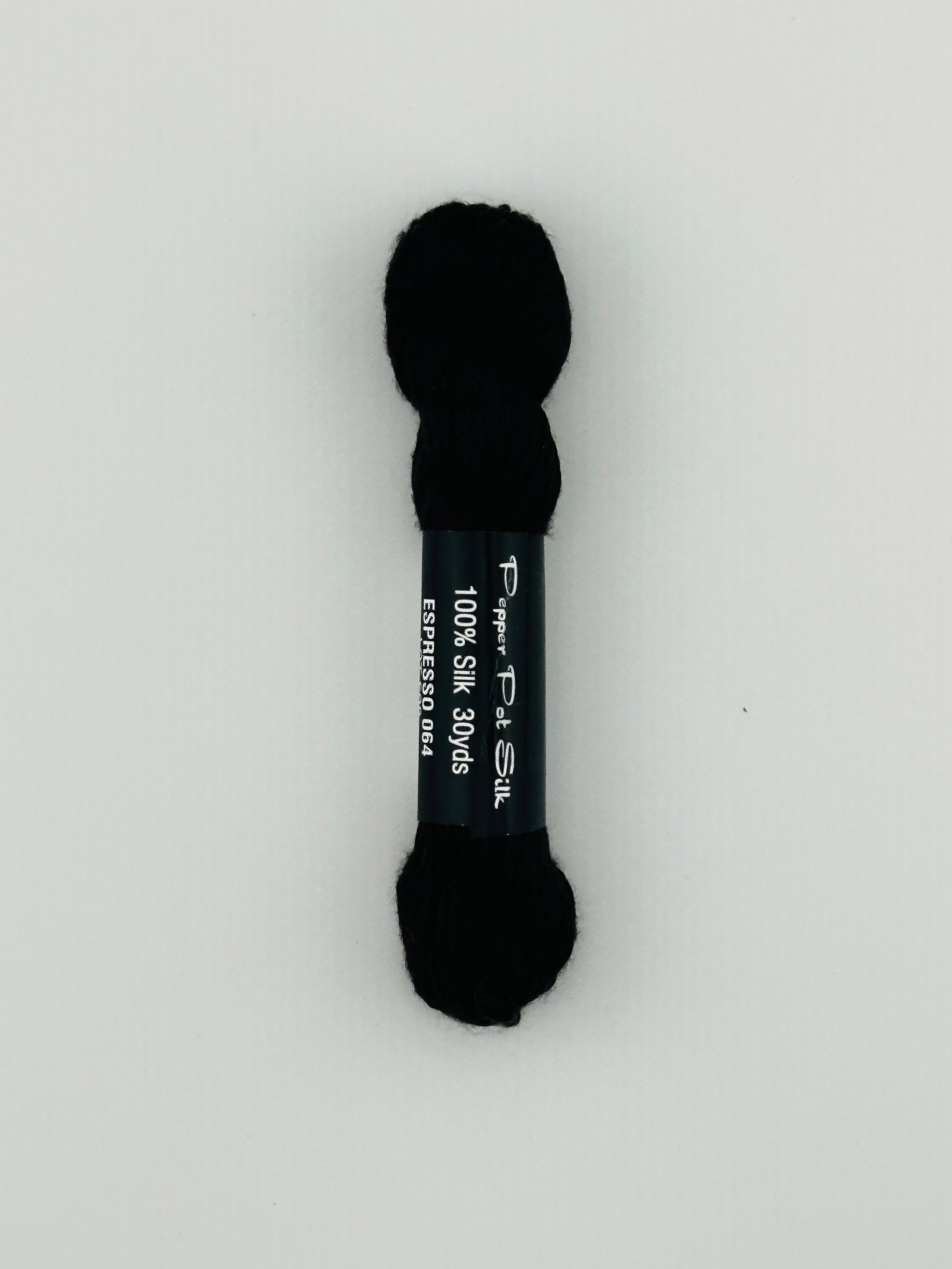 30 yard skein of Pepper Pot Silk needlepoint thread in espresso 064, with black and white label lying flat on white background