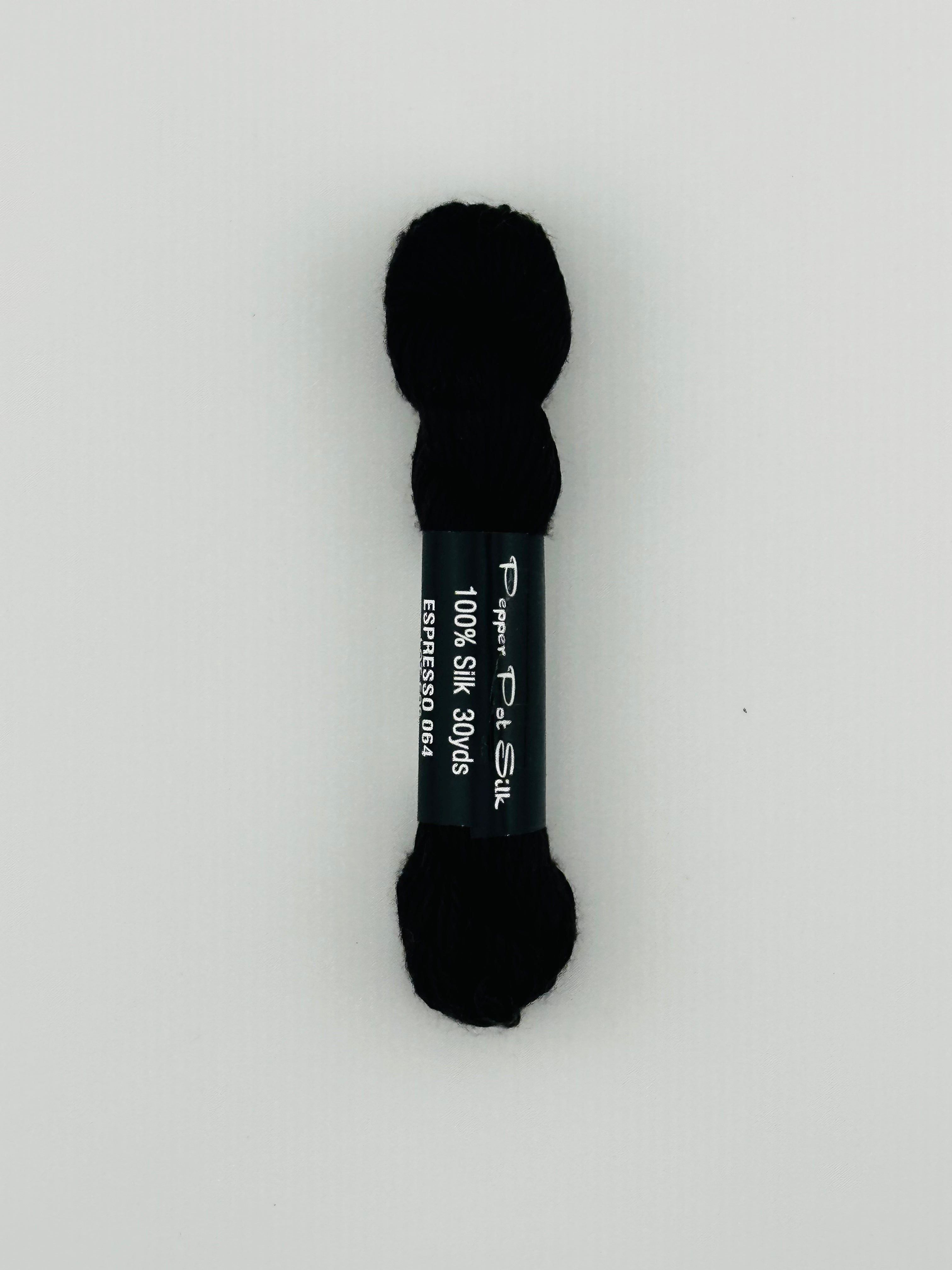 30 yard skein of Pepper Pot Silk needlepoint thread in espresso 064, with black and white label lying flat on white background