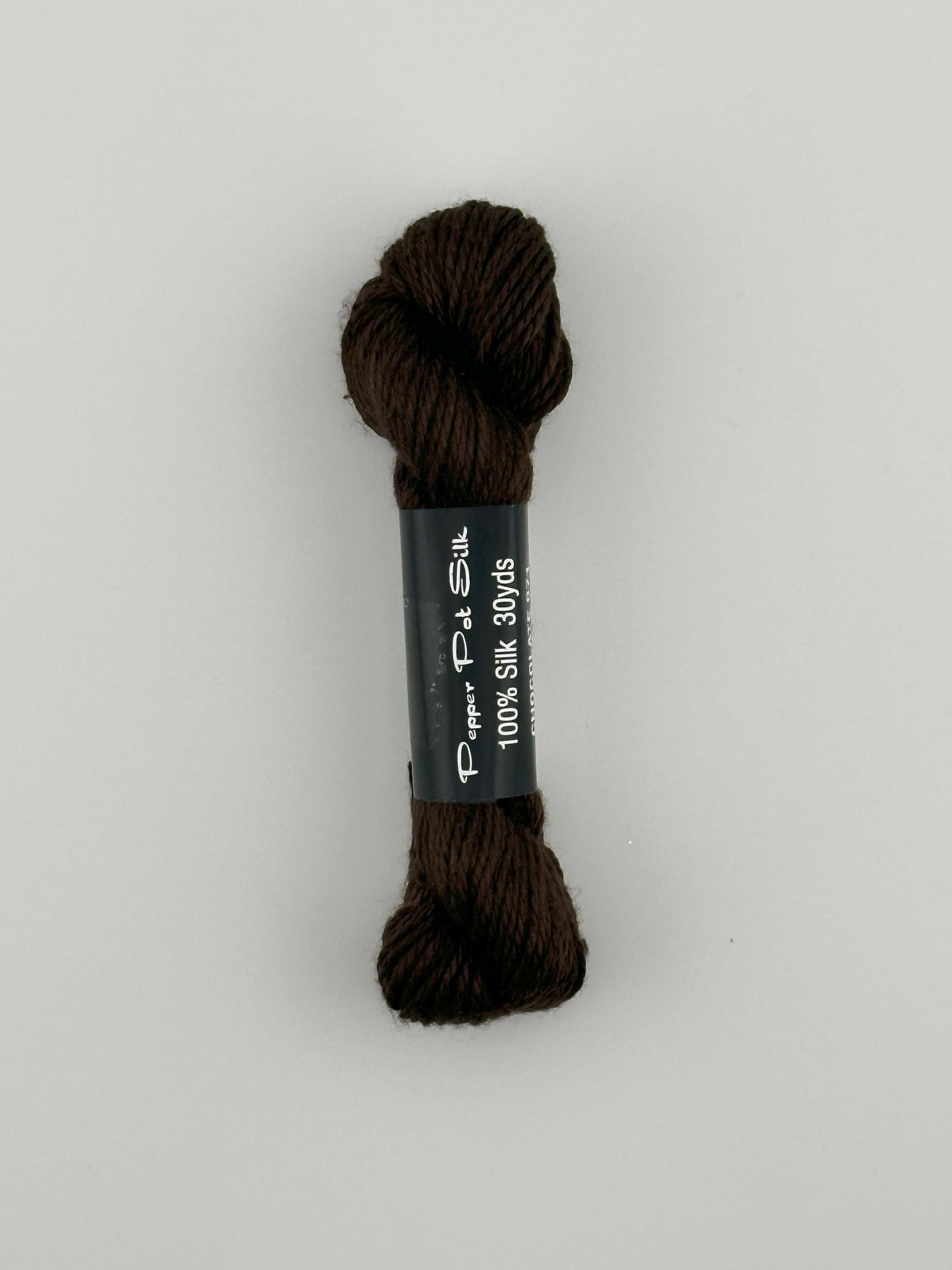 30 yard skein of Pepper Pot Silk needlepoint thread in chocolate 071 brown with black and white label lying flat on white background