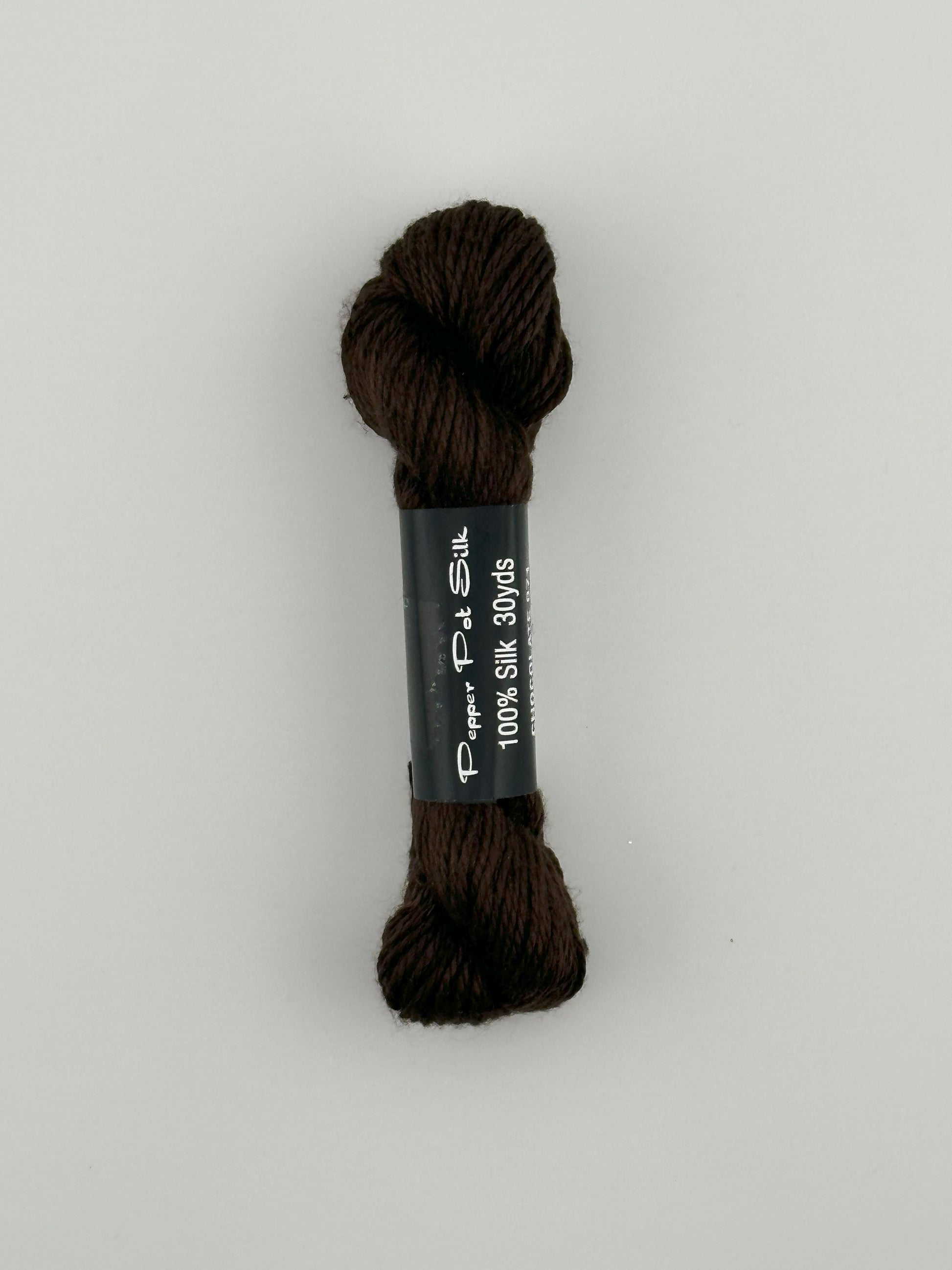 30 yard skein of Pepper Pot Silk needlepoint thread in chocolate 071 brown with black and white label lying flat on white background