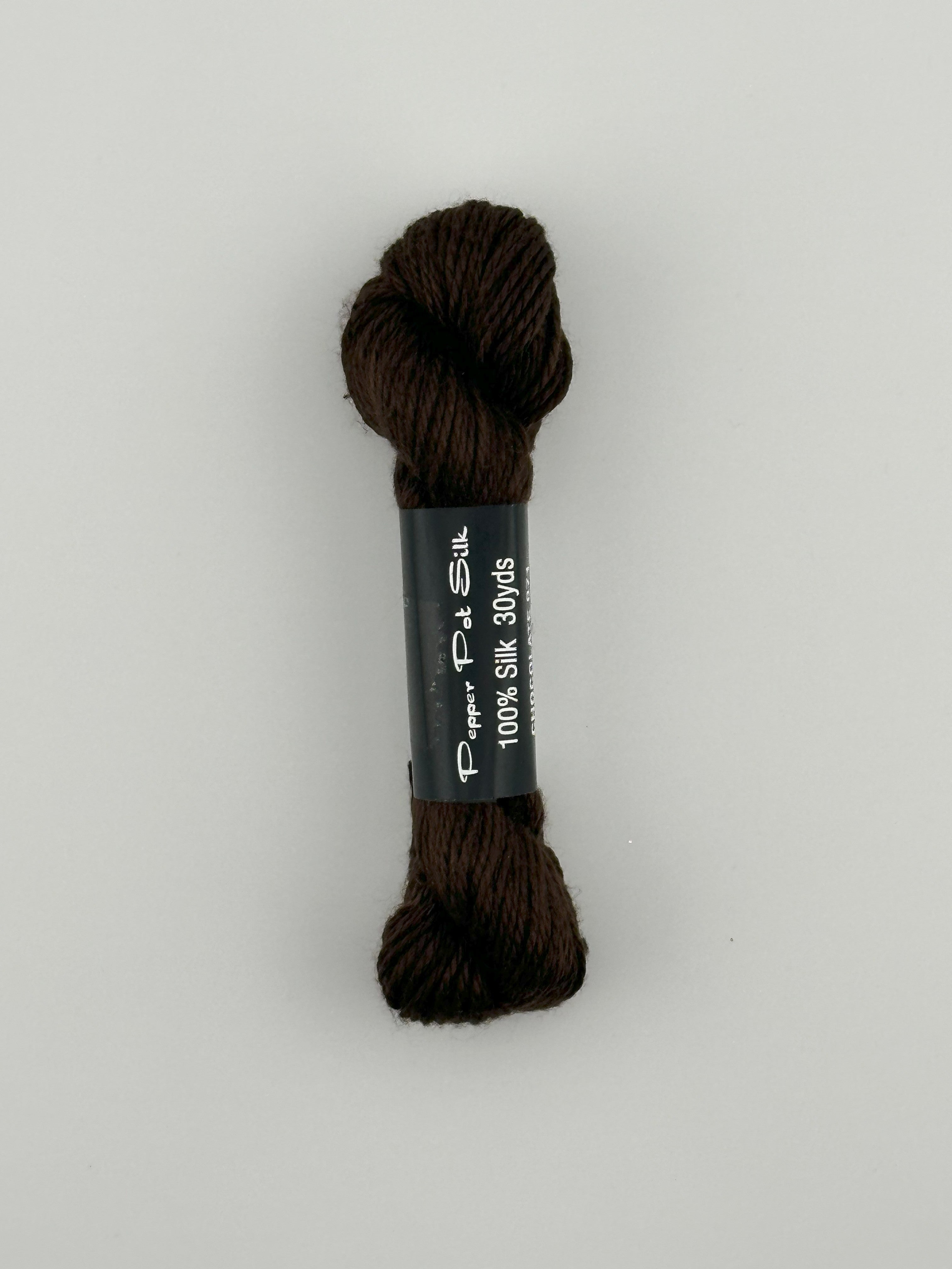 30 yard skein of Pepper Pot Silk needlepoint thread in chocolate 071 brown with black and white label lying flat on white background