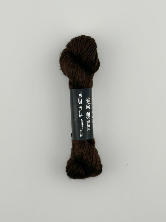 30 yard skein of Pepper Pot Silk needlepoint thread in chocolate 071 brown with black and white label lying flat on white background