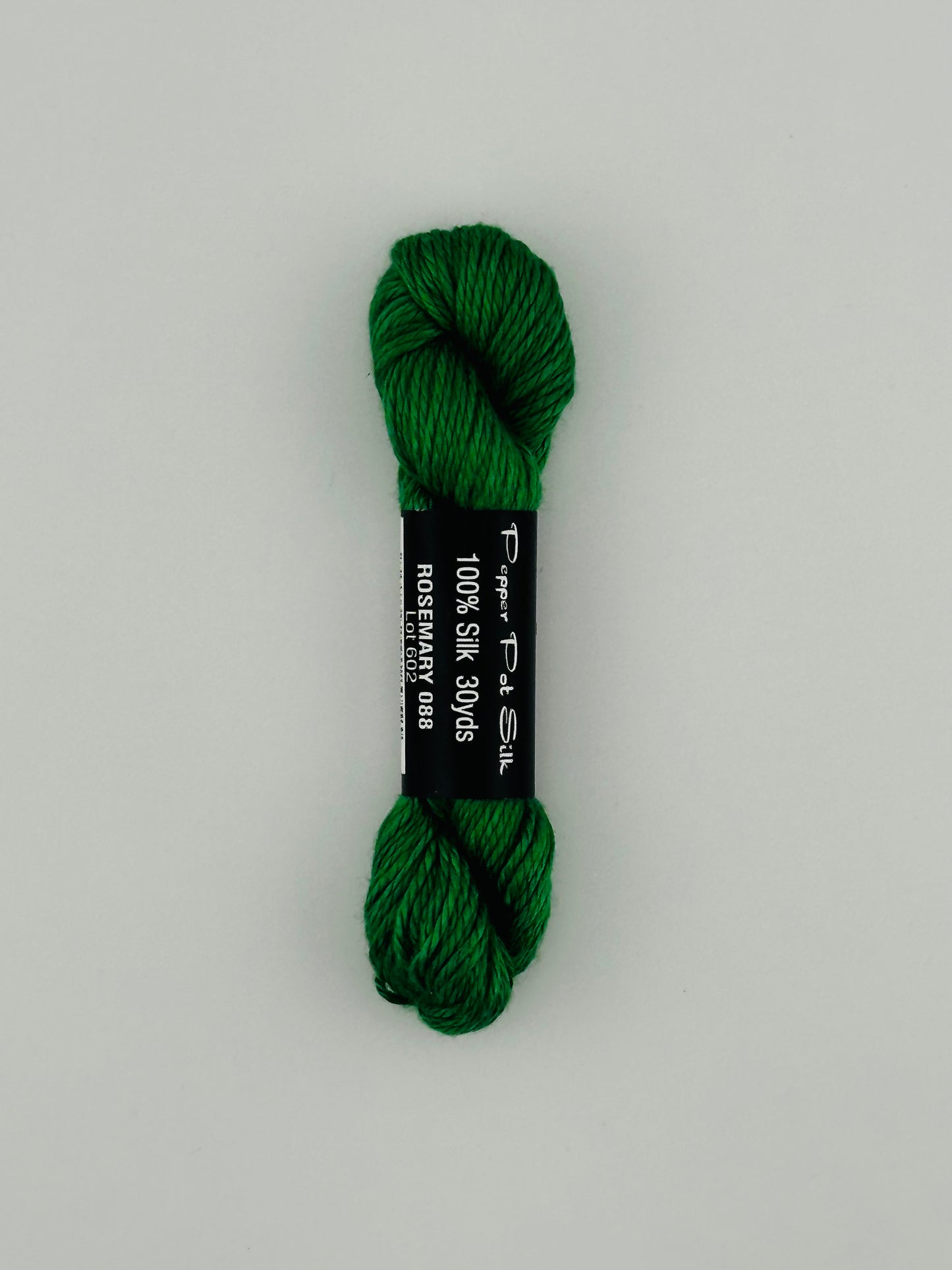 30 yard skein of Pepper Pot Silk needlepoint thread in rosemary 088, with black and white label lying flat on white background