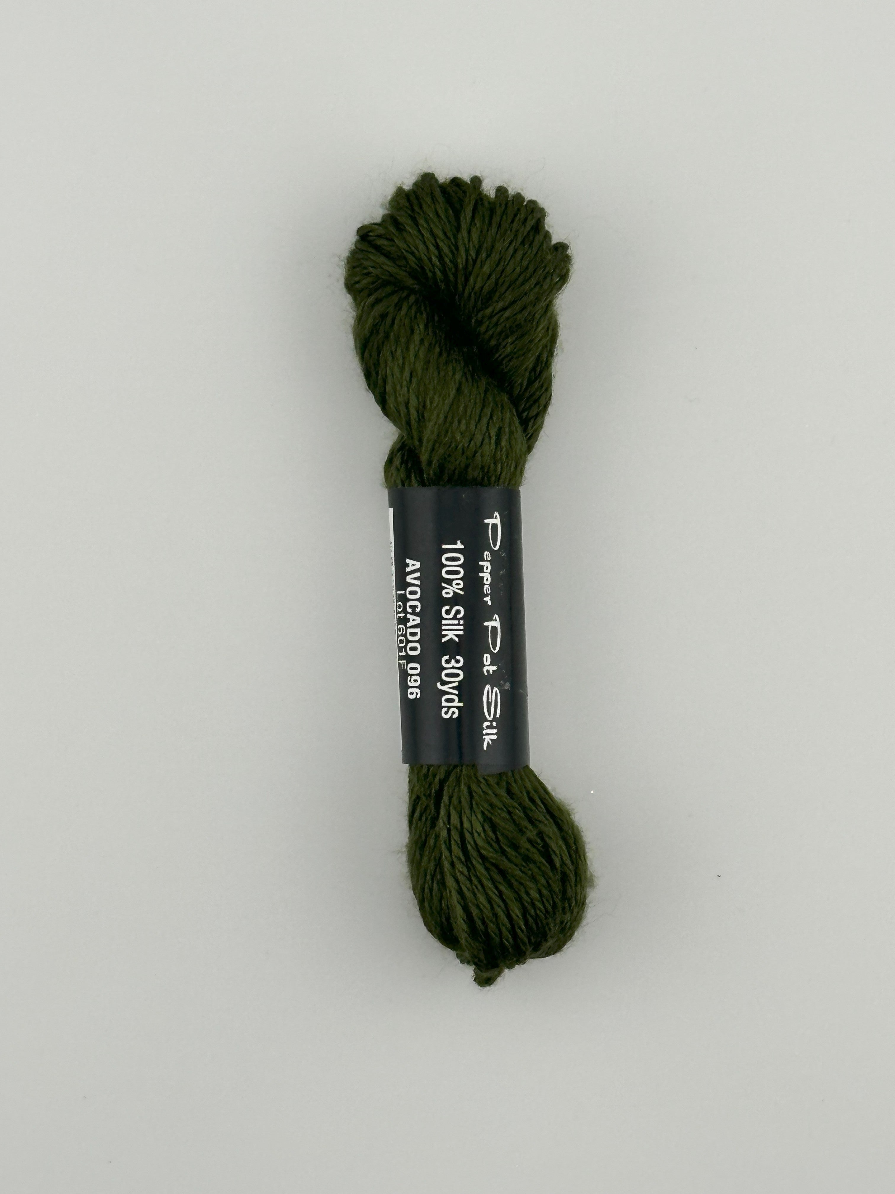 30 yard skein of Pepper Pot Silk needlepoint thread in Avocado 096 green, with black and white label lying flat on white background