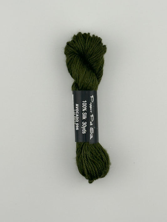 30 yard skein of Pepper Pot Silk needlepoint thread in Avocado 096 green, with black and white label lying flat on white background