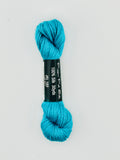 30 yard skein of Pepper Pot Silk needlepoint thread in jello 103, with black and white label lying flat on white background