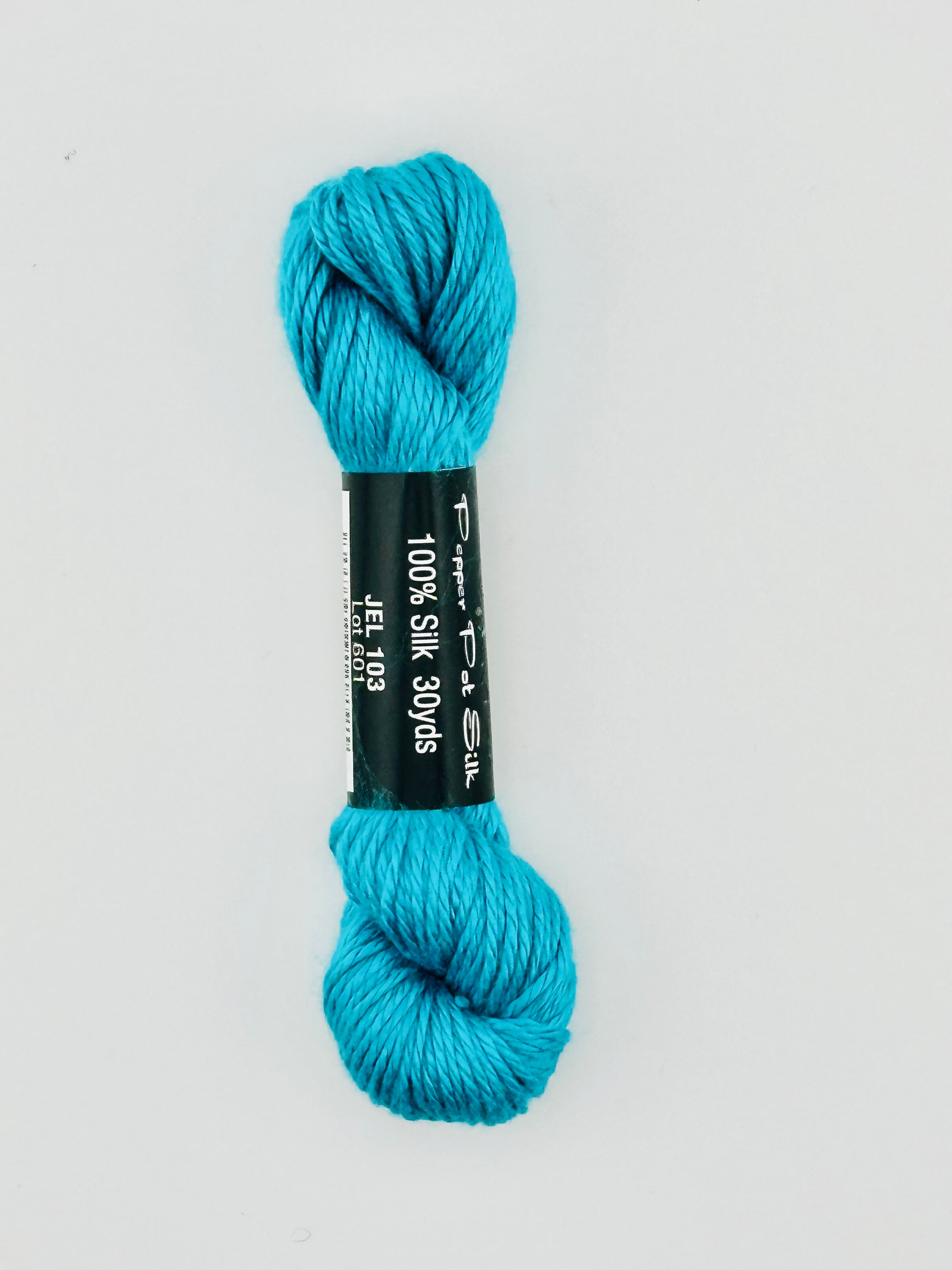30 yard skein of Pepper Pot Silk needlepoint thread in jello 103, with black and white label lying flat on white background