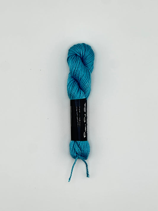 30 yard skein of Pepper Pot Silk needlepoint thread in ceramic blue 107 with black and white label lying flat on white background