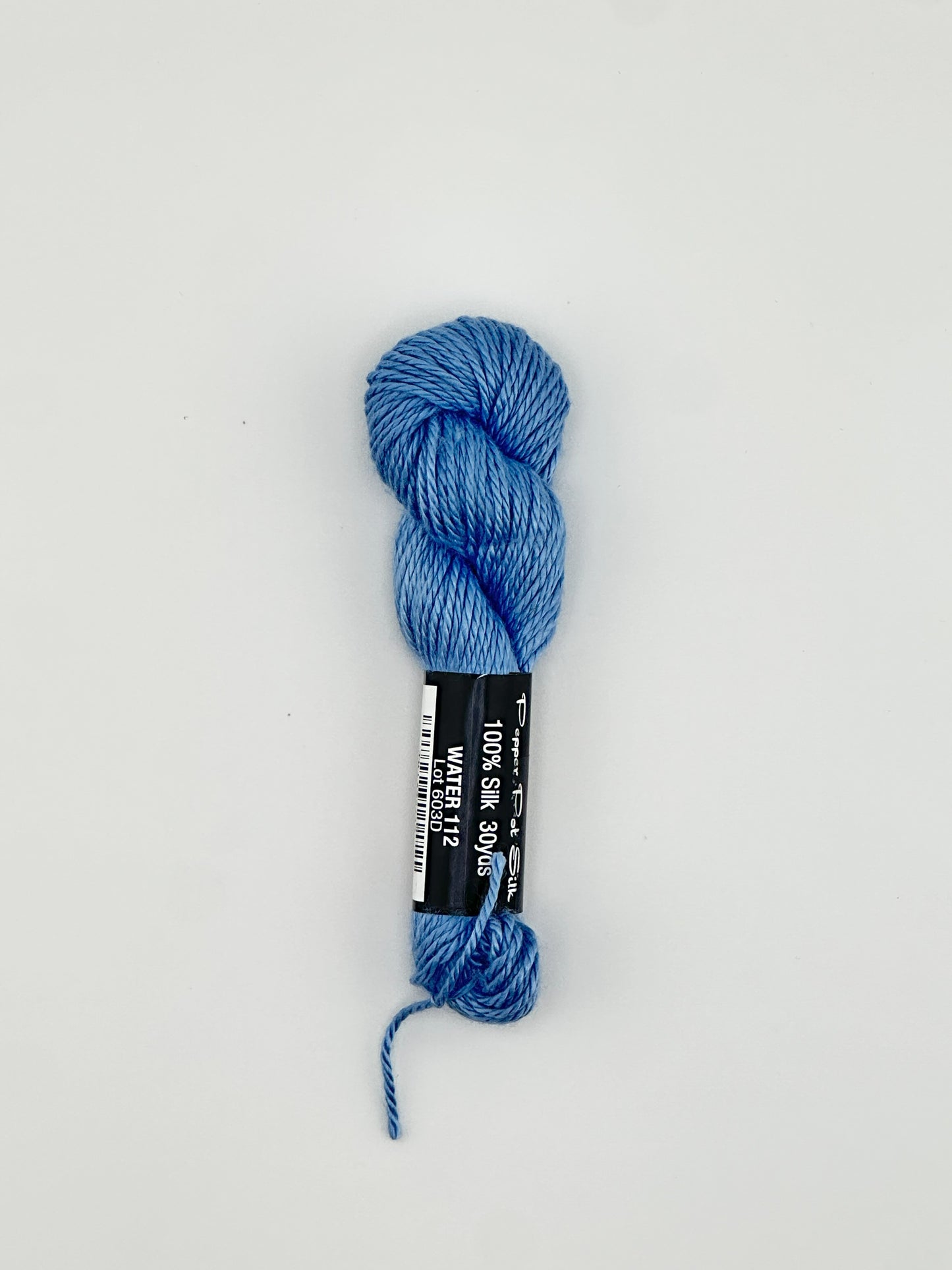 30 yard skein of Pepper Pot Silk needlepoint thread in water blue 112 with black and white label lying flat on white background