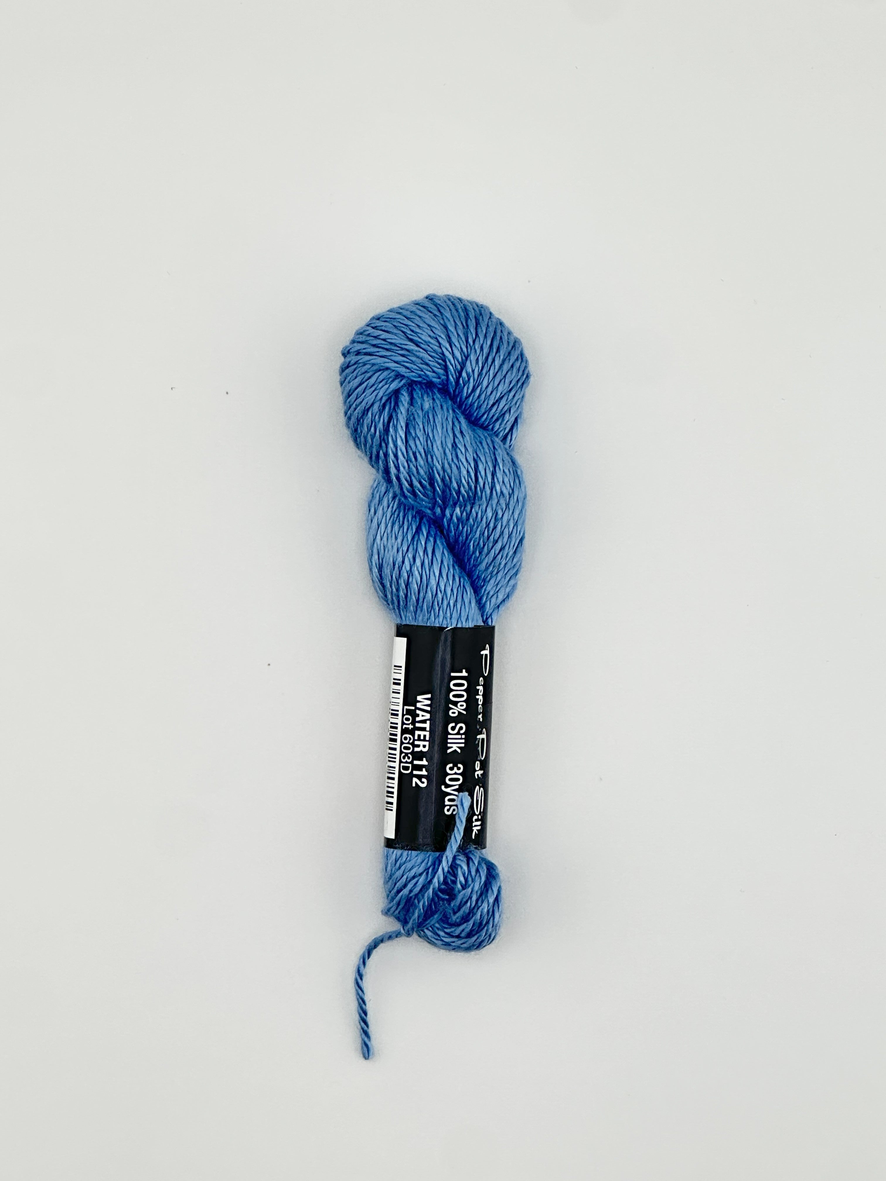 30 yard skein of Pepper Pot Silk needlepoint thread in water blue 112 with black and white label lying flat on white background