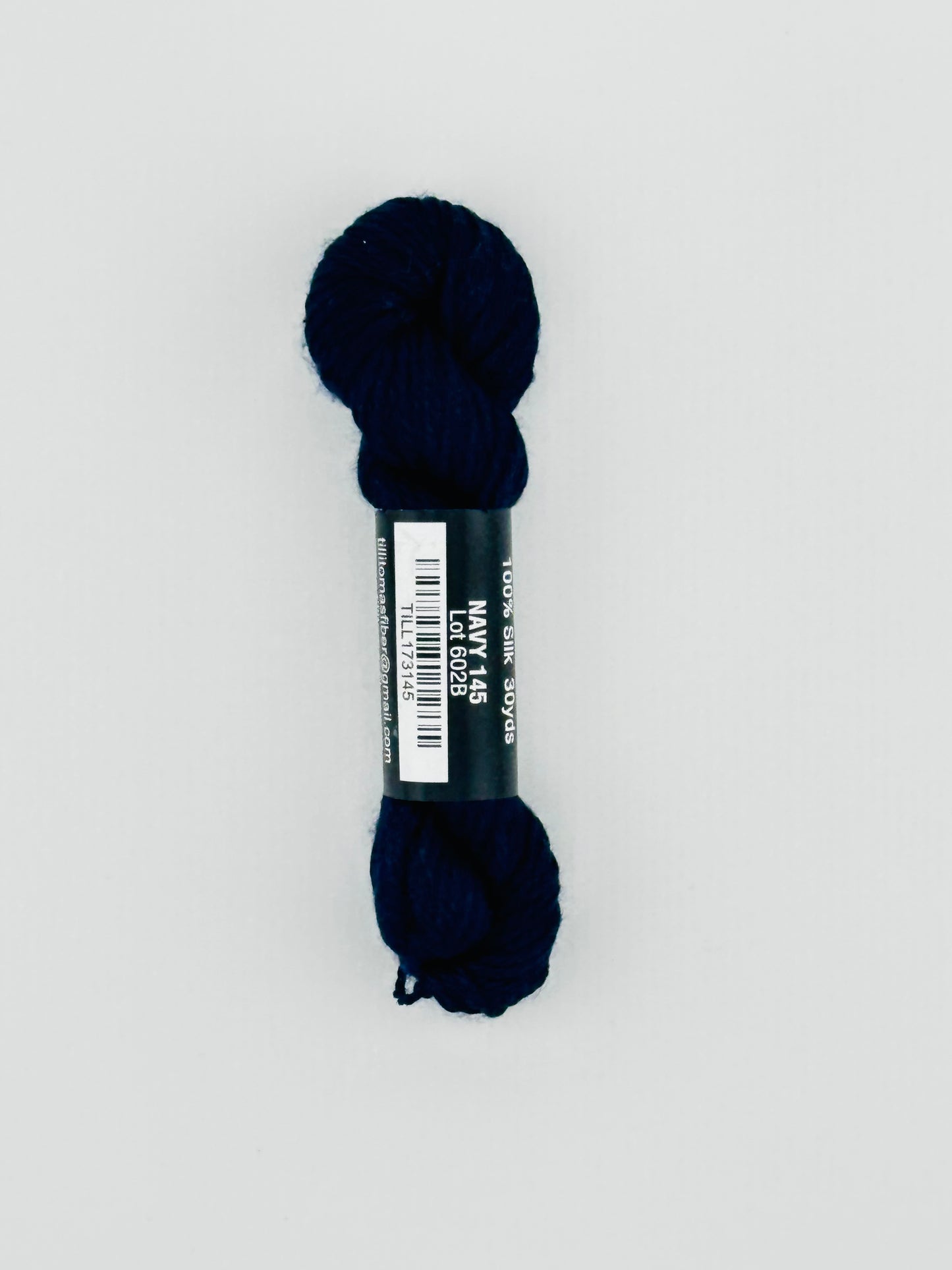 30 yard skein of Pepper Pot Silk needlepoint thread in navy 145, with black and white label lying flat on white background