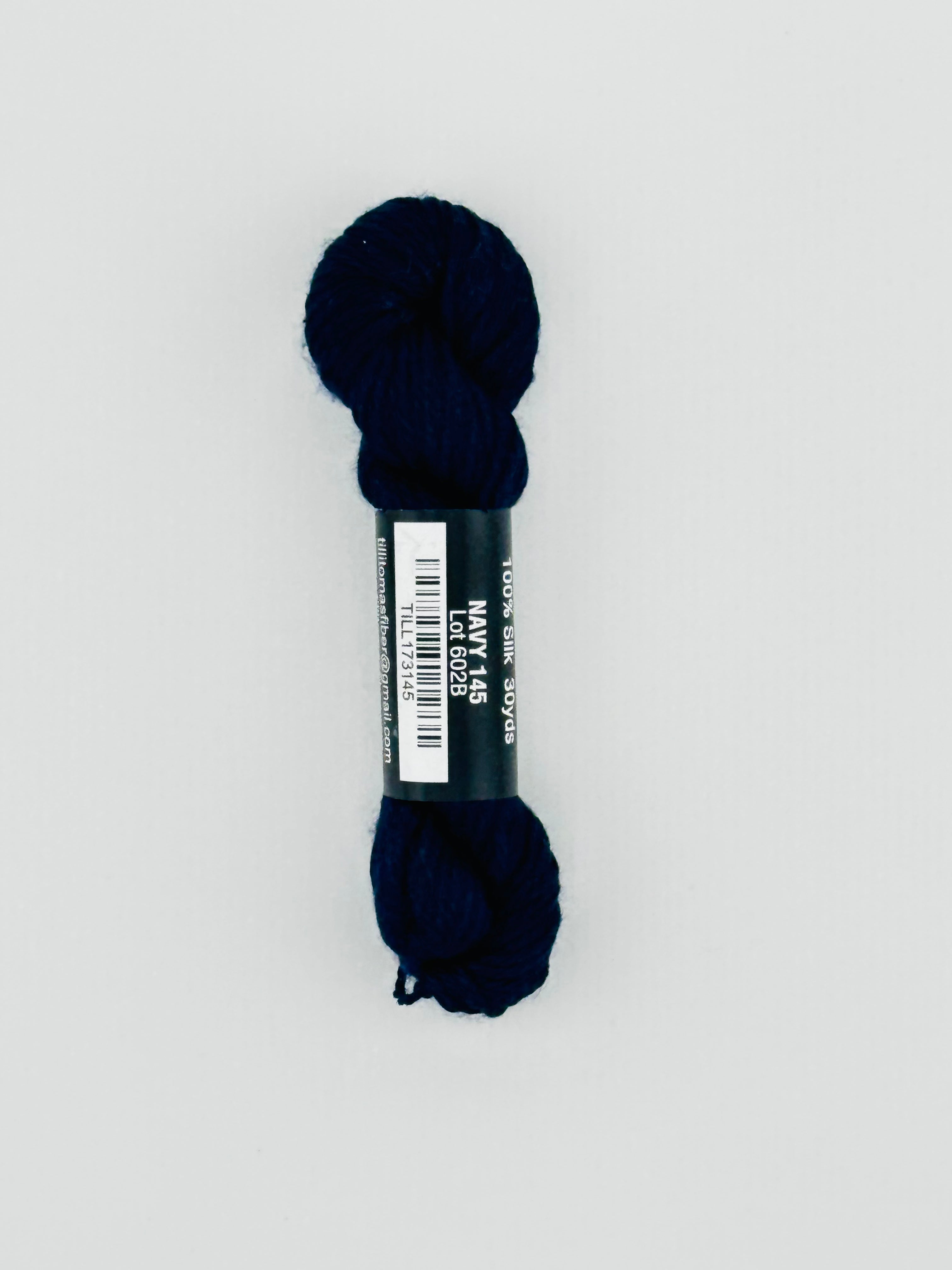 30 yard skein of Pepper Pot Silk needlepoint thread in navy 145, with black and white label lying flat on white background
