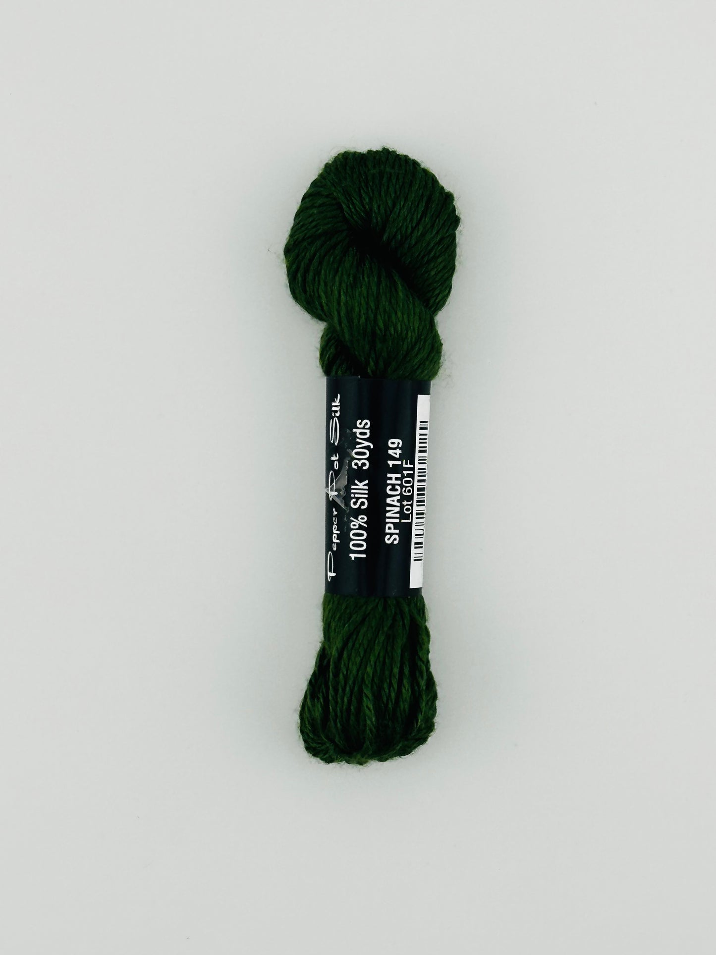 30 yard skein of Pepper Pot Silk needlepoint thread in spinach 149, with black and white label lying flat on white background
