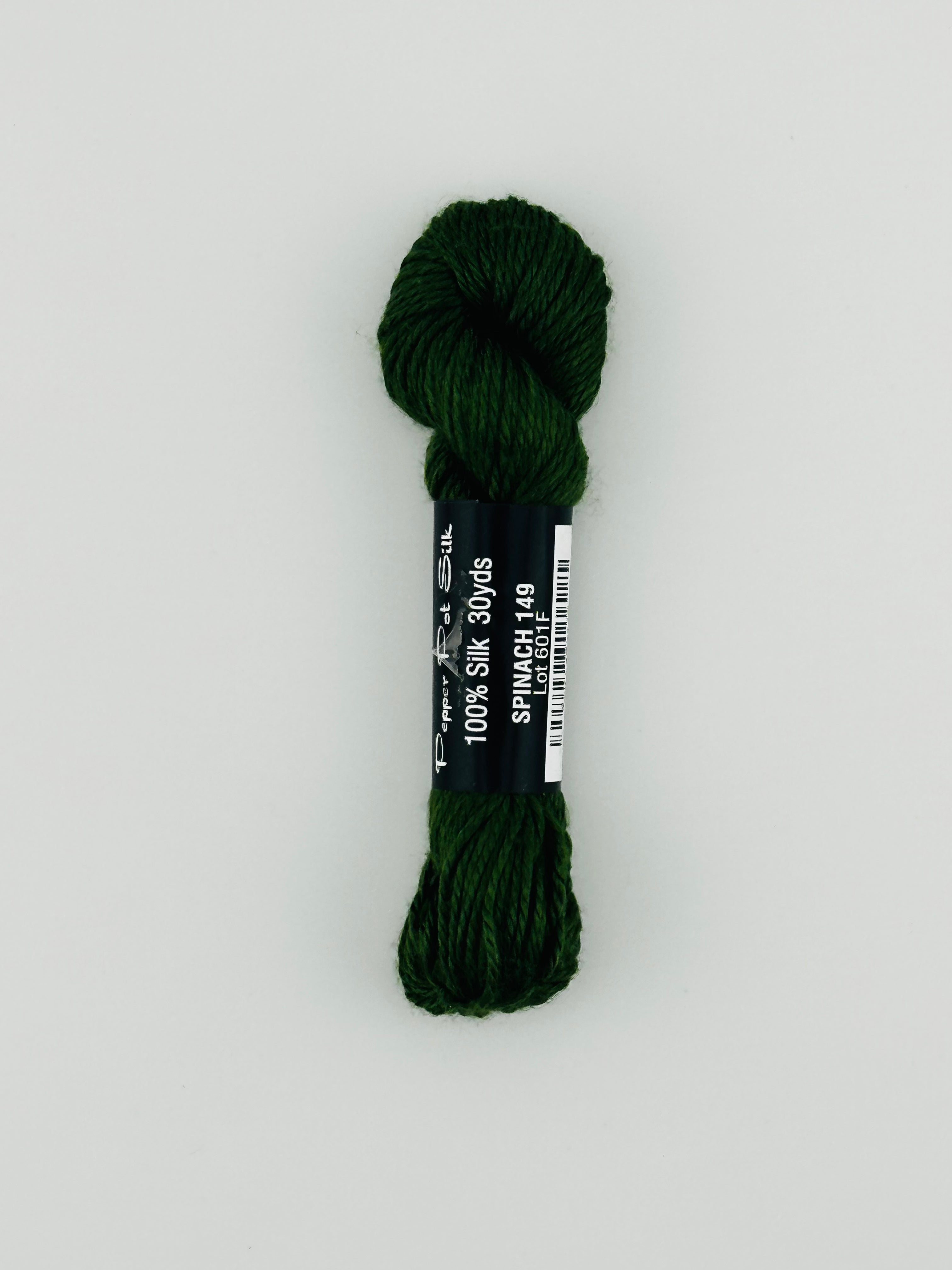 30 yard skein of Pepper Pot Silk needlepoint thread in spinach 149, with black and white label lying flat on white background