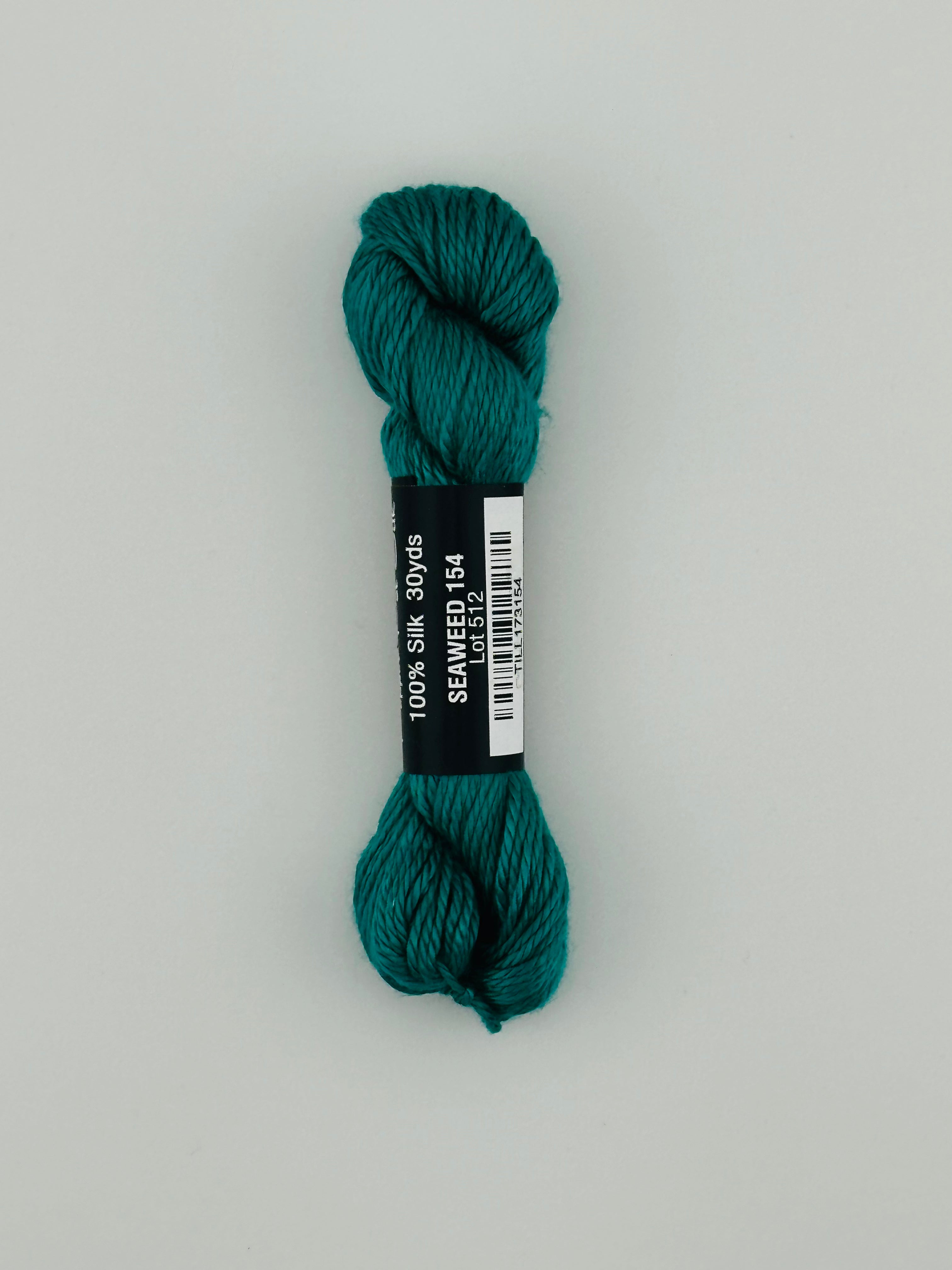 30 yard skein of Pepper Pot Silk needlepoint thread in seaweed 154, with black and white label lying flat on white background