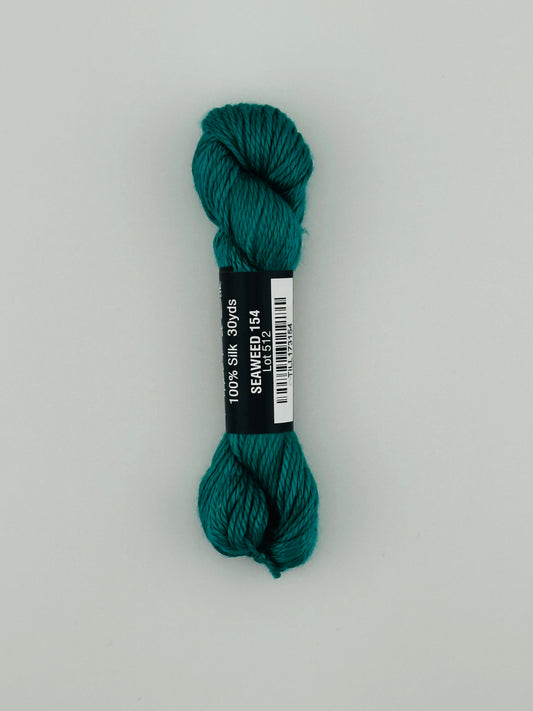30 yard skein of Pepper Pot Silk needlepoint thread in seaweed 154, with black and white label lying flat on white background