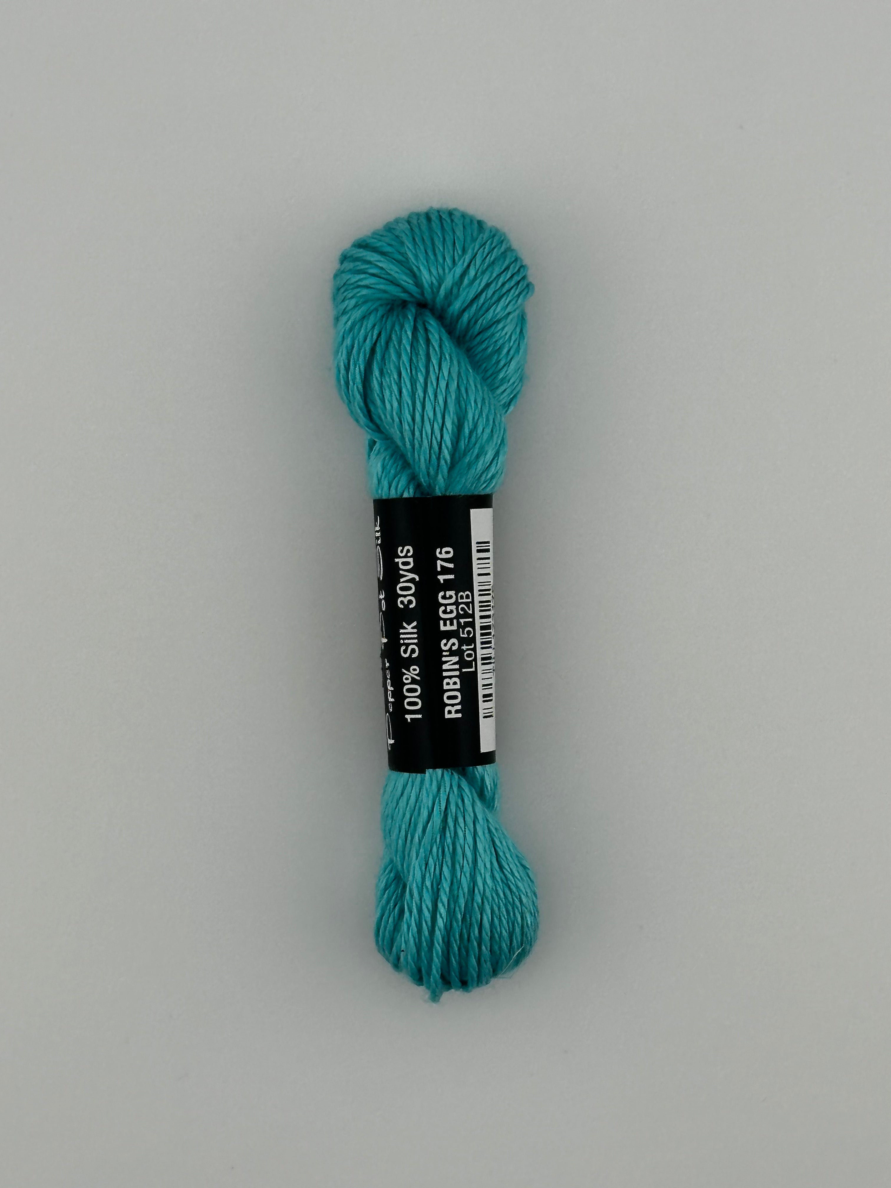30 yard skein of Pepper Pot Silk needlepoint thread in robins egg 176, with black and white label lying flat on white background