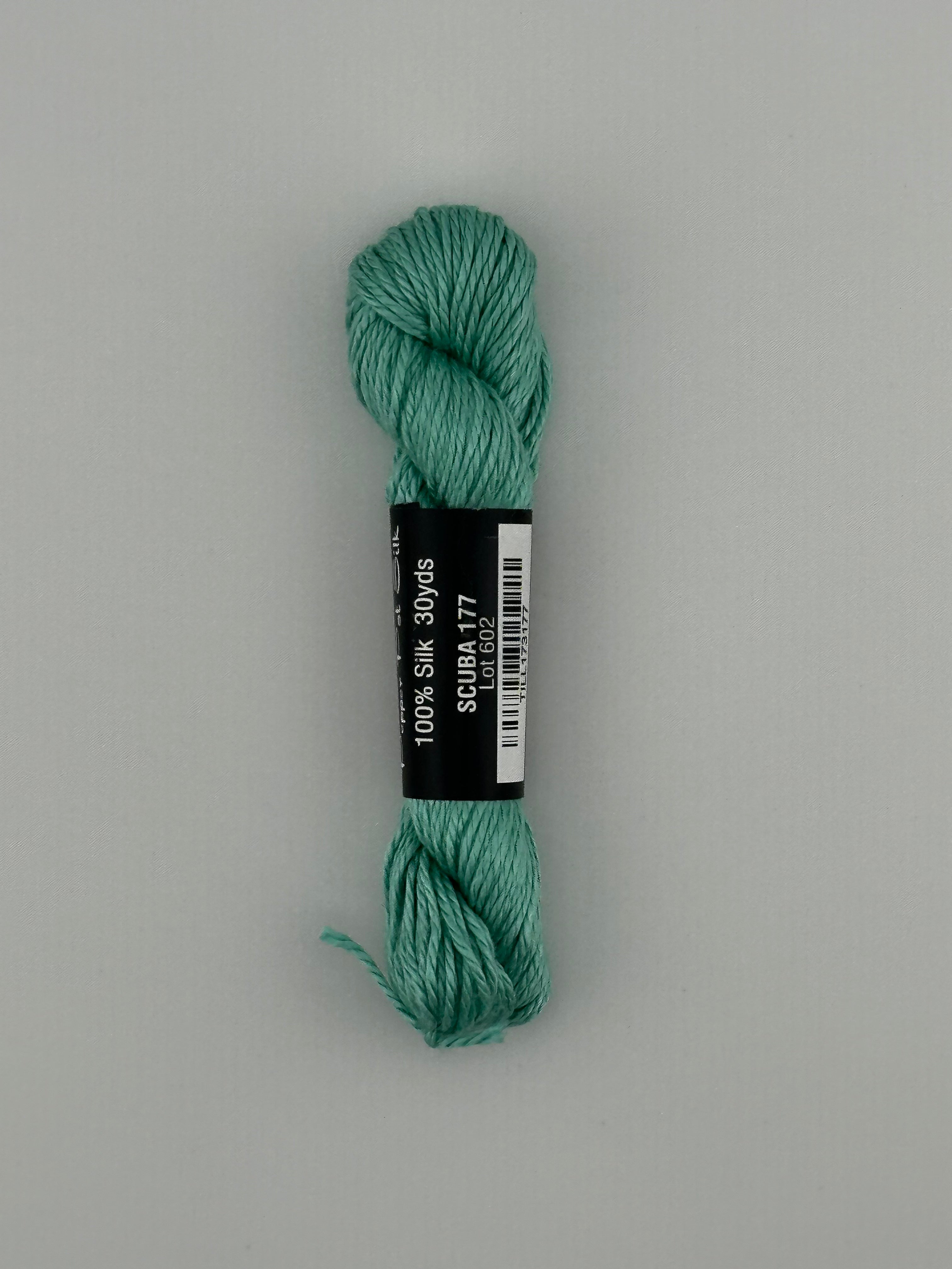 30 yard skein of Pepper Pot Silk needlepoint thread in scuba 177, with black and white label lying flat on white background