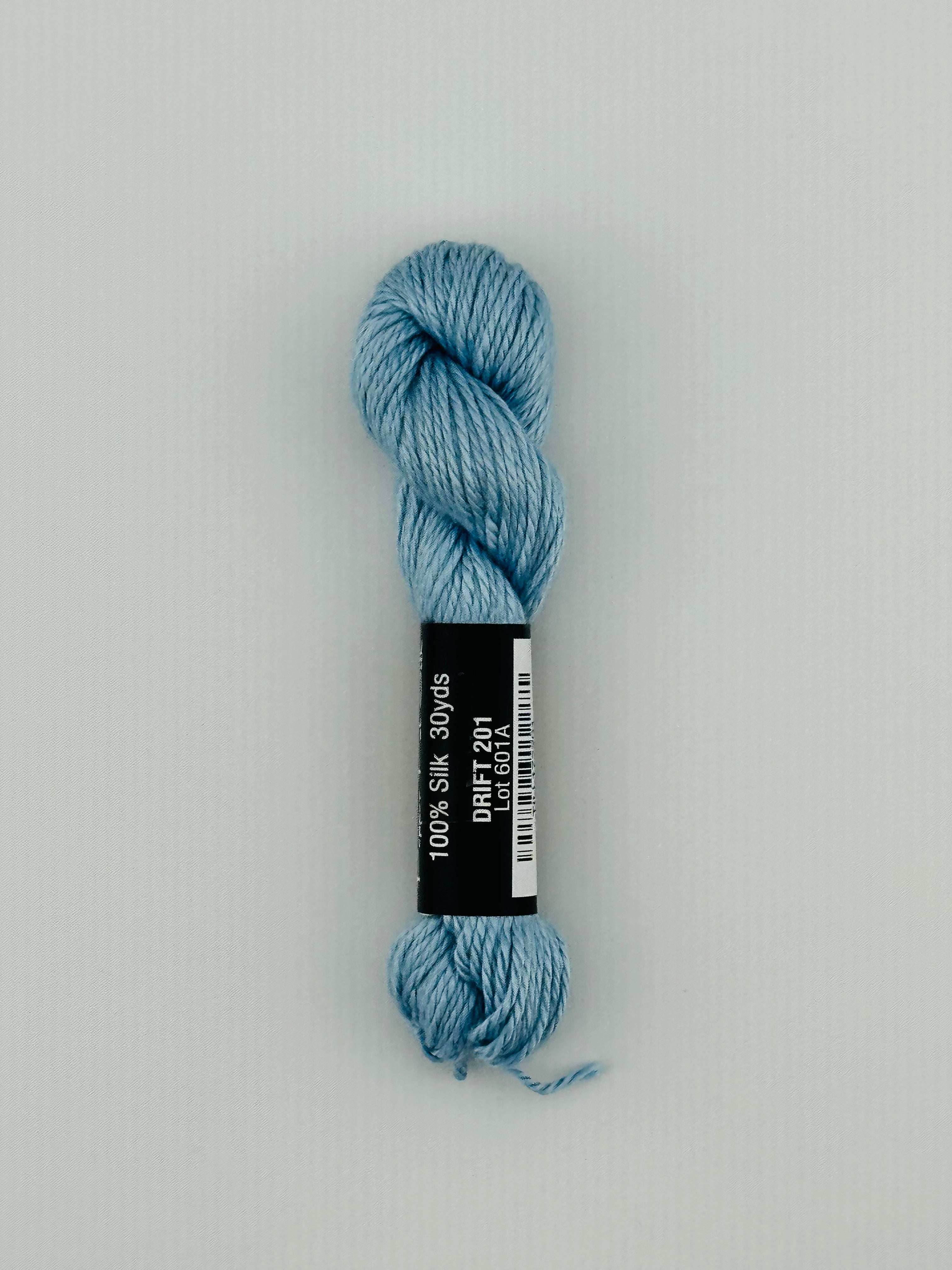 30 yard skein of Pepper Pot Silk needlepoint thread in drift 201, with black and white label lying flat on white background