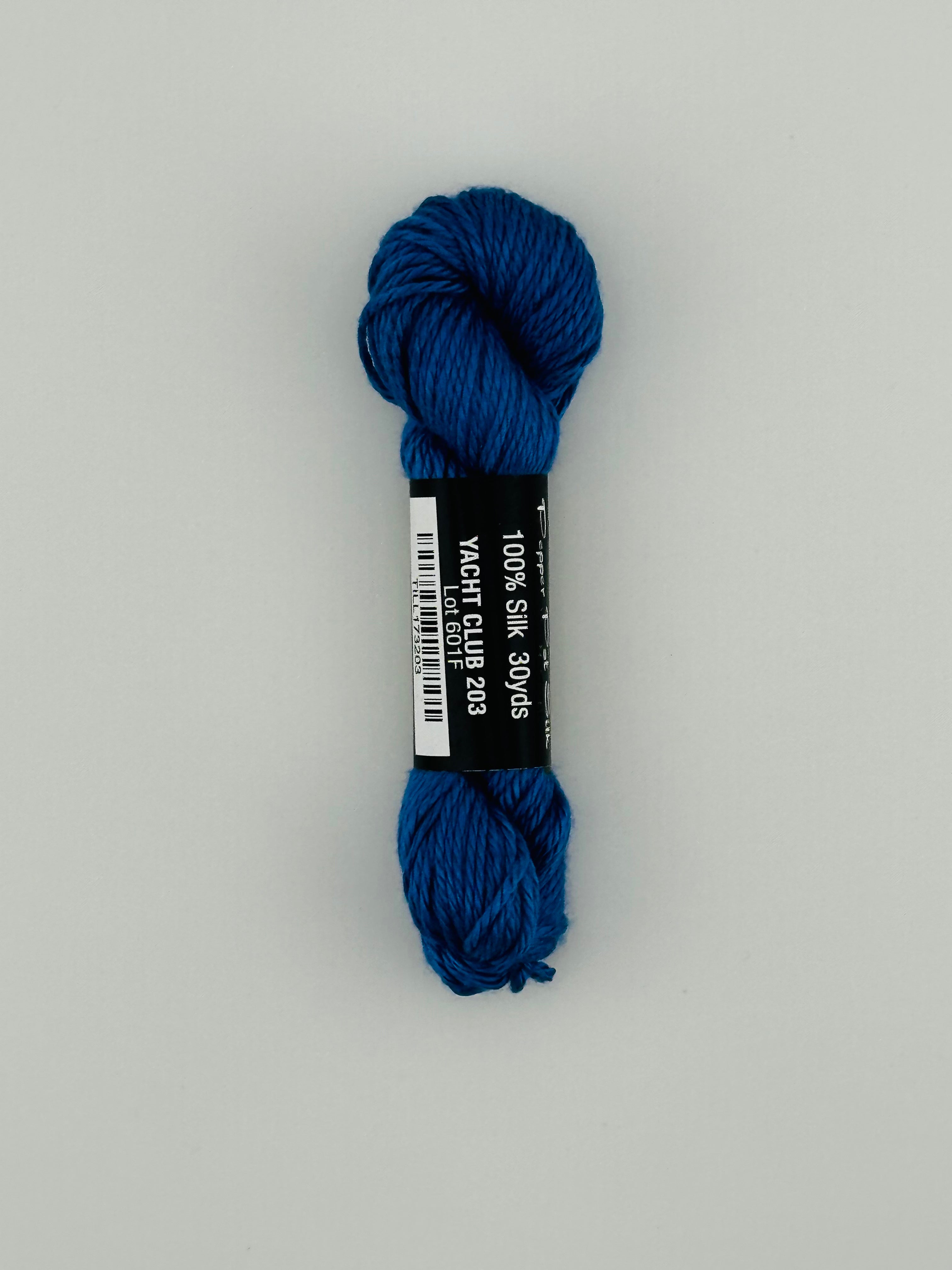 30 yard skein of Pepper Pot Silk needlepoint thread in yacht club 203, with black and white label lying flat on white background