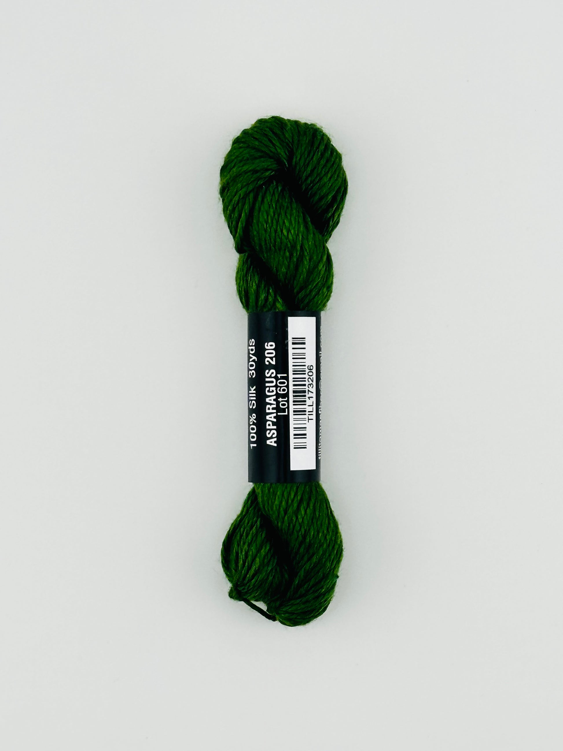 30 yard skein of Pepper Pot Silk needlepoint thread in Avocado 096 green, with black and white label lying flat on white background
