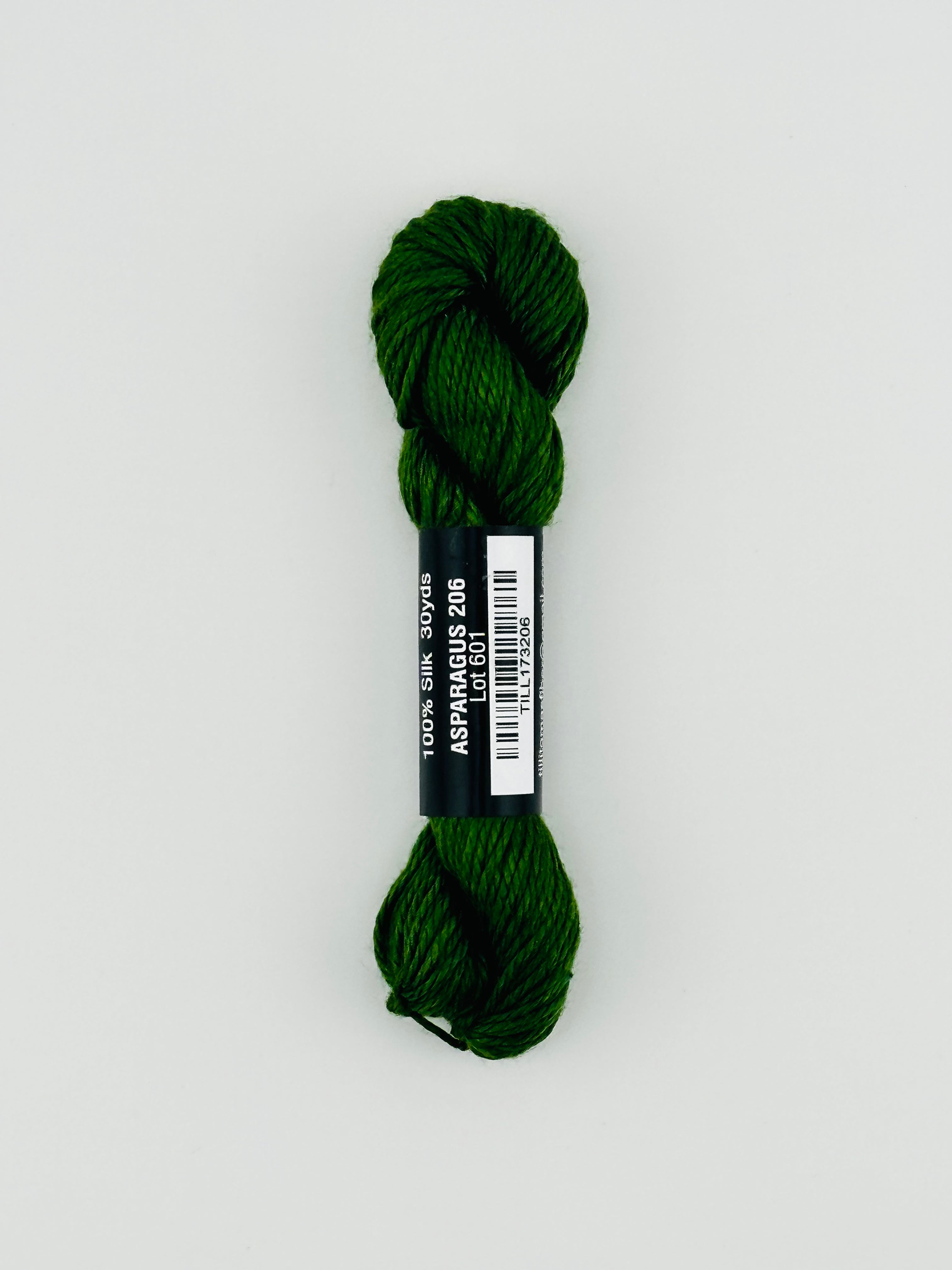 30 yard skein of Pepper Pot Silk needlepoint thread in Avocado 096 green, with black and white label lying flat on white background