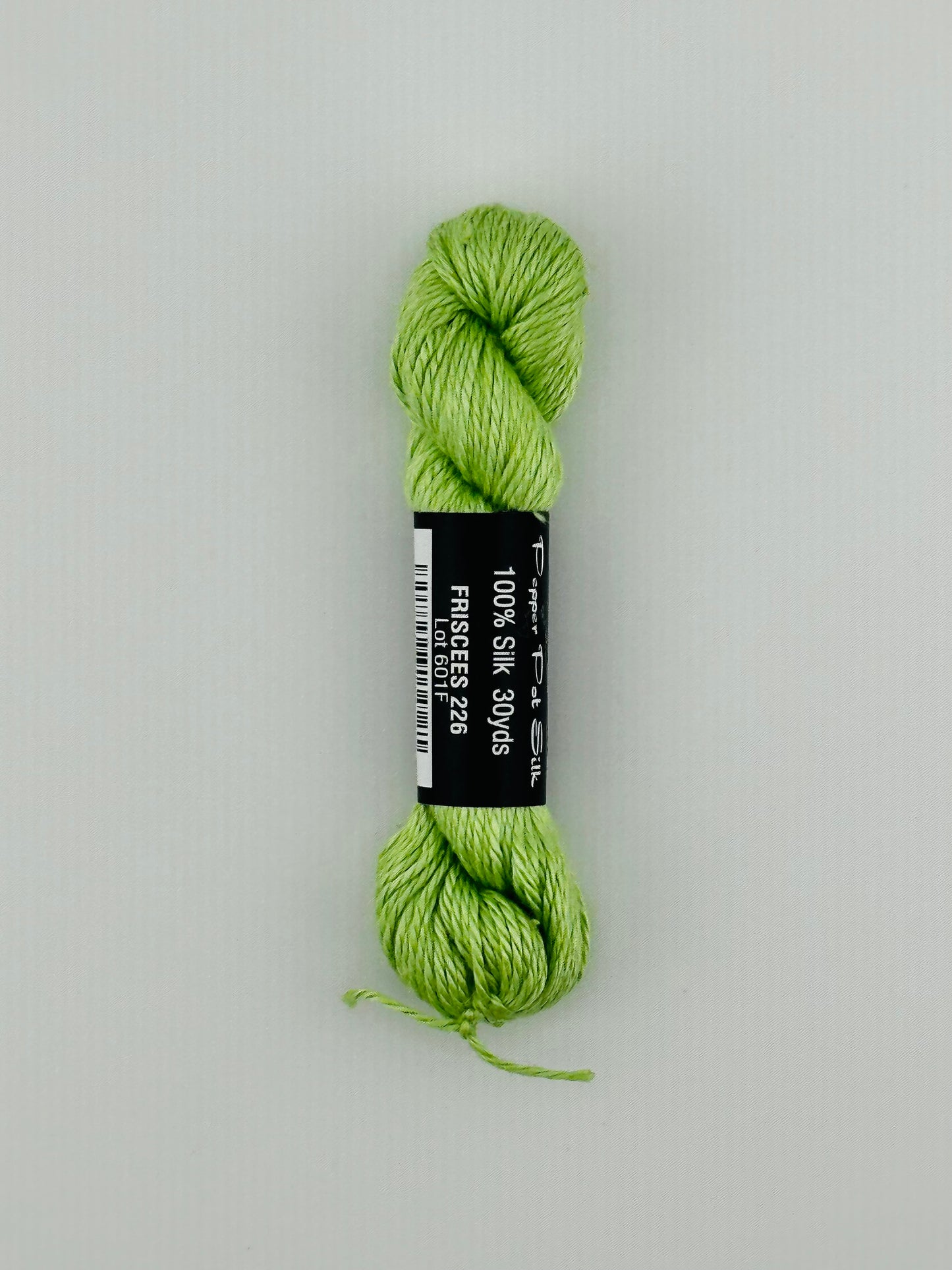 30 yard skein of Pepper Pot Silk needlepoint thread in friscees 226, with black and white label lying flat on white background
