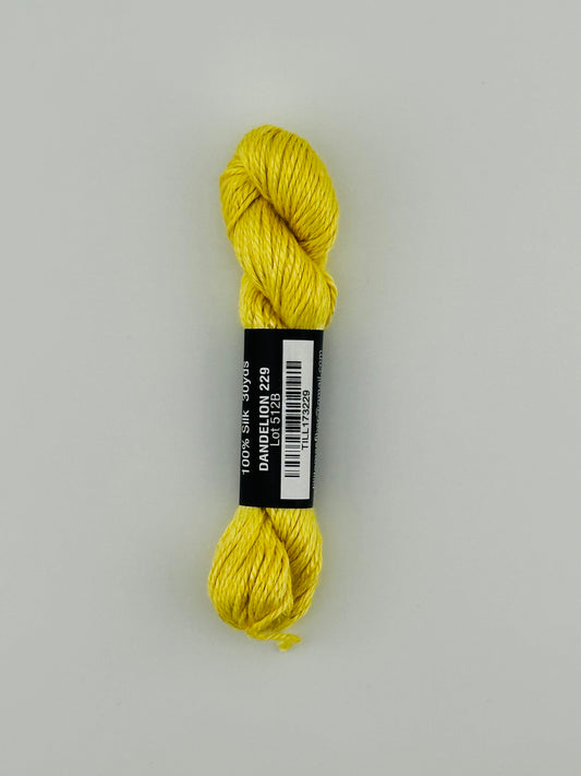30 yard skein of Pepper Pot Silk needlepoint thread in dandelion, with black and white label lying flat on white background