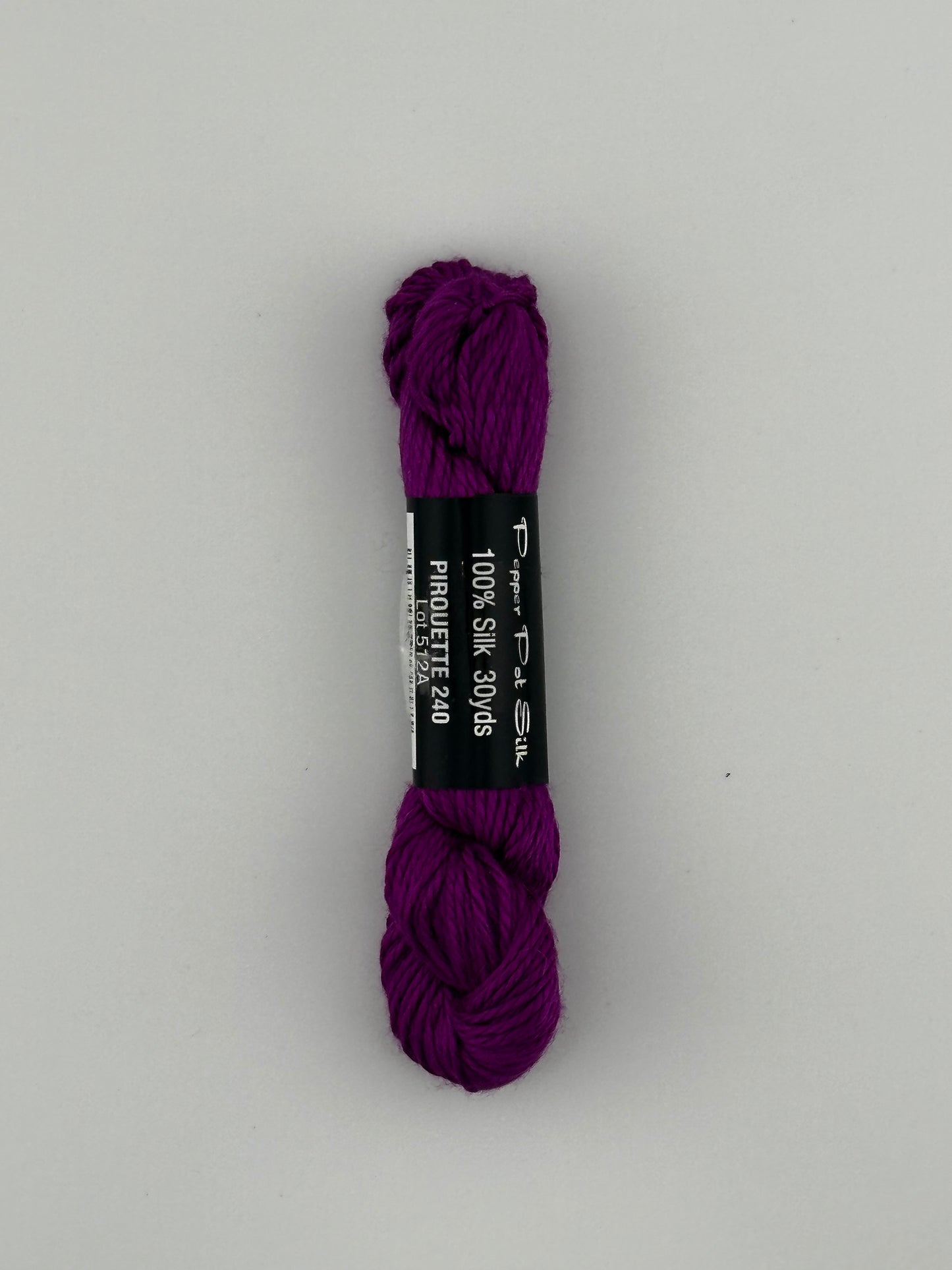 30 yard skein of Pepper Pot Silk needlepoint thread in piroutte 240, with black and white label lying flat on white background