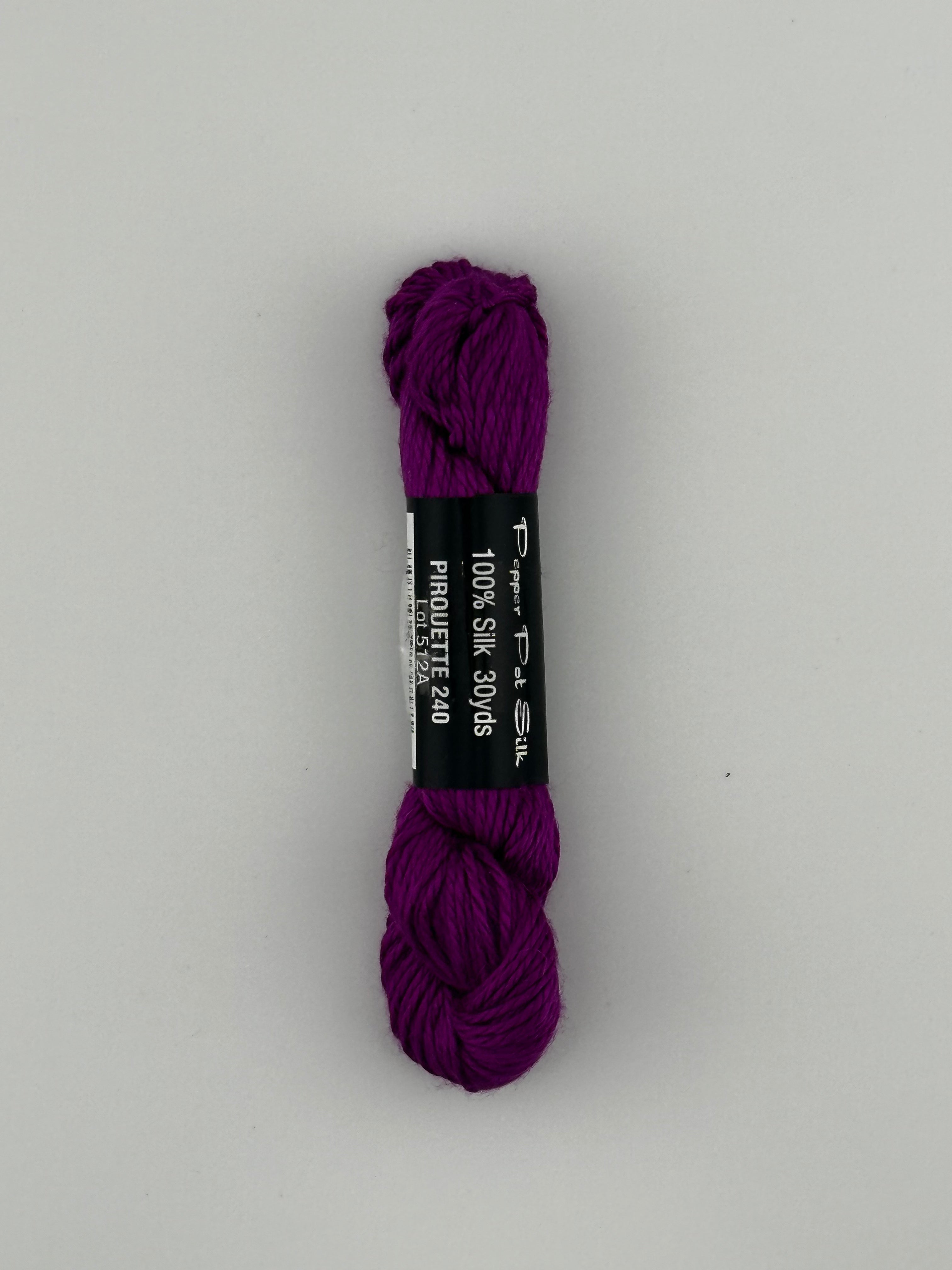 30 yard skein of Pepper Pot Silk needlepoint thread in piroutte 240, with black and white label lying flat on white background