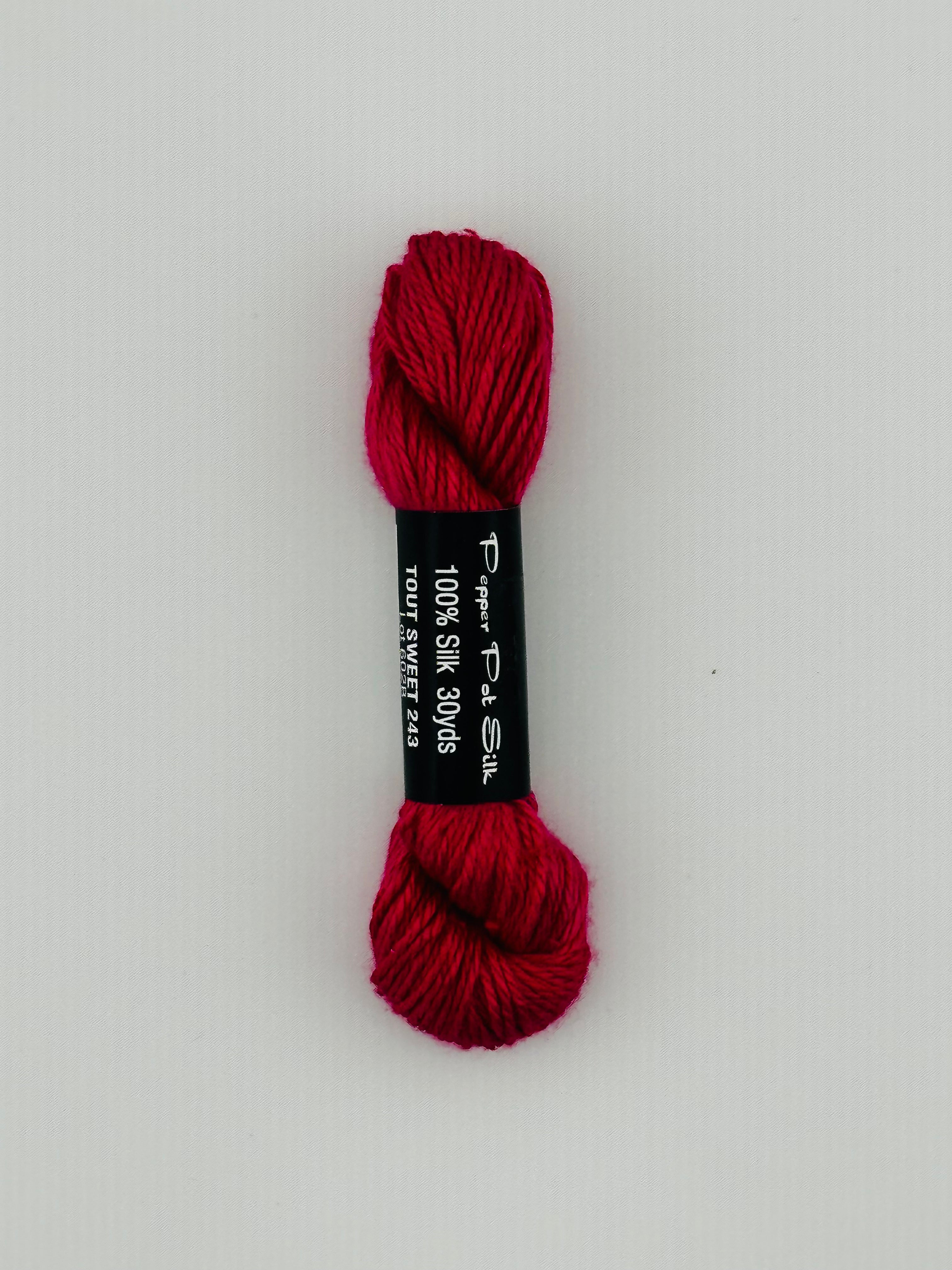 30 yard skein of Pepper Pot Silk needlepoint thread in tout sweet 243, with black and white label lying flat on white background