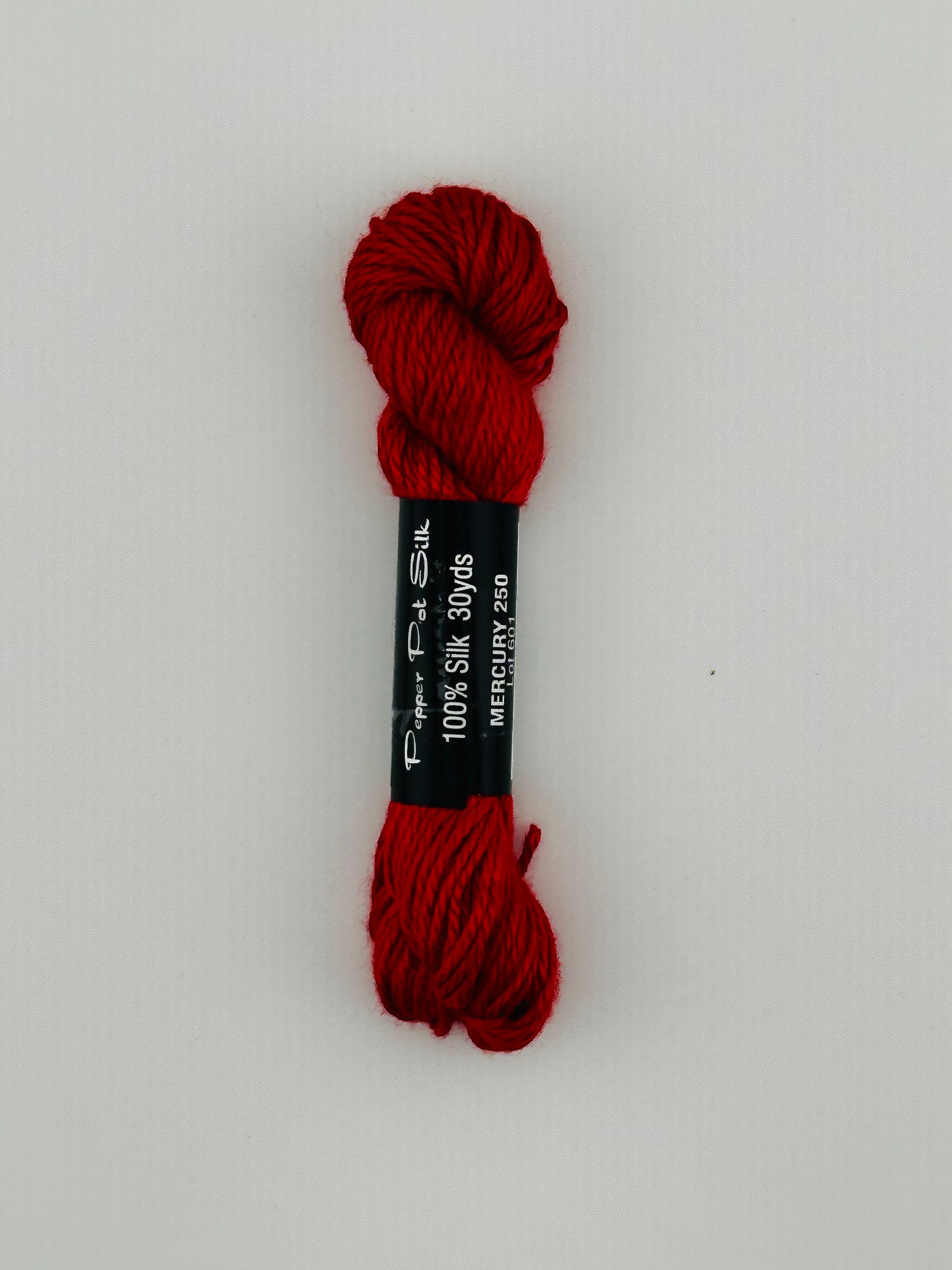 30 yard skein of Pepper Pot Silk needlepoint thread in mercury 250, with black and white label lying flat on white background