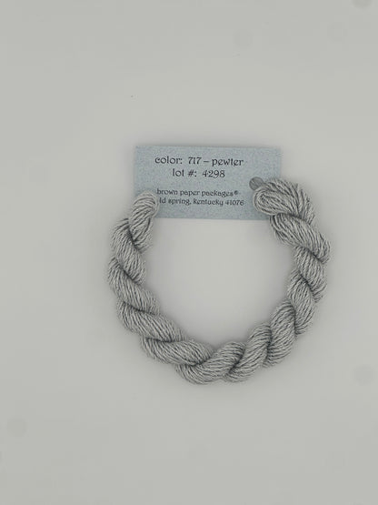 30 yard skein of Stardust Silk and Ivory needlepoint thread in Pewter 717 grey, with light blue label lying flat on white background