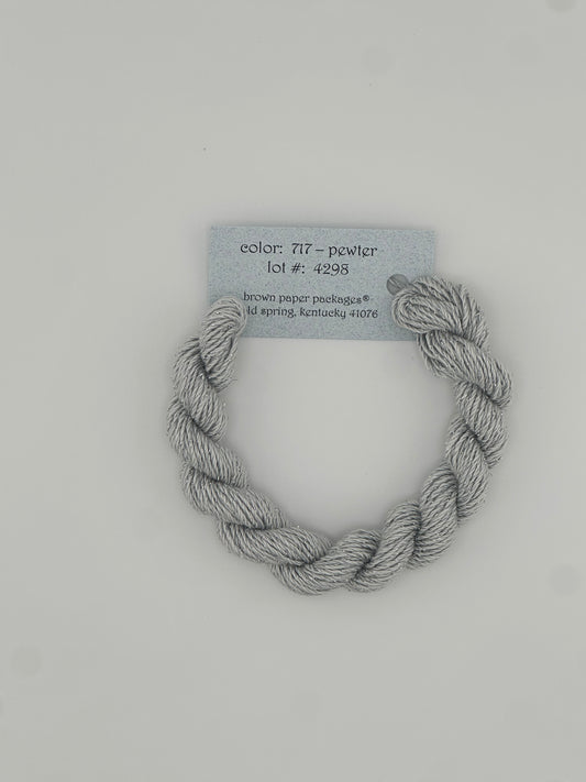 30 yard skein of Stardust Silk and Ivory needlepoint thread in Pewter 717 grey, with light blue label lying flat on white background