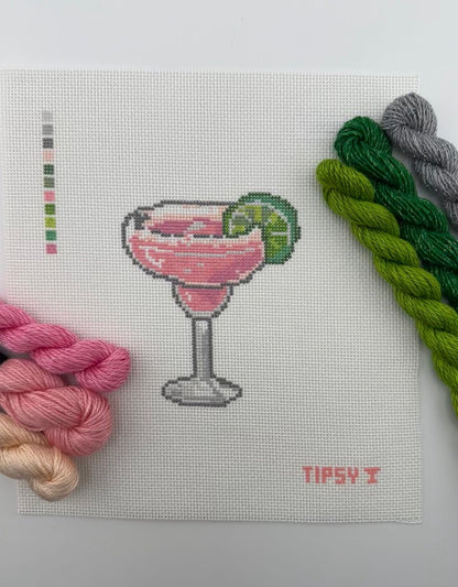 A square 18 mesh needlepoint canvas featuring a pink margarita cocktail in a glass with a lime wedge, on a white background with a small red TIPSY  text at the bottom right and matching threads on top of canvas.